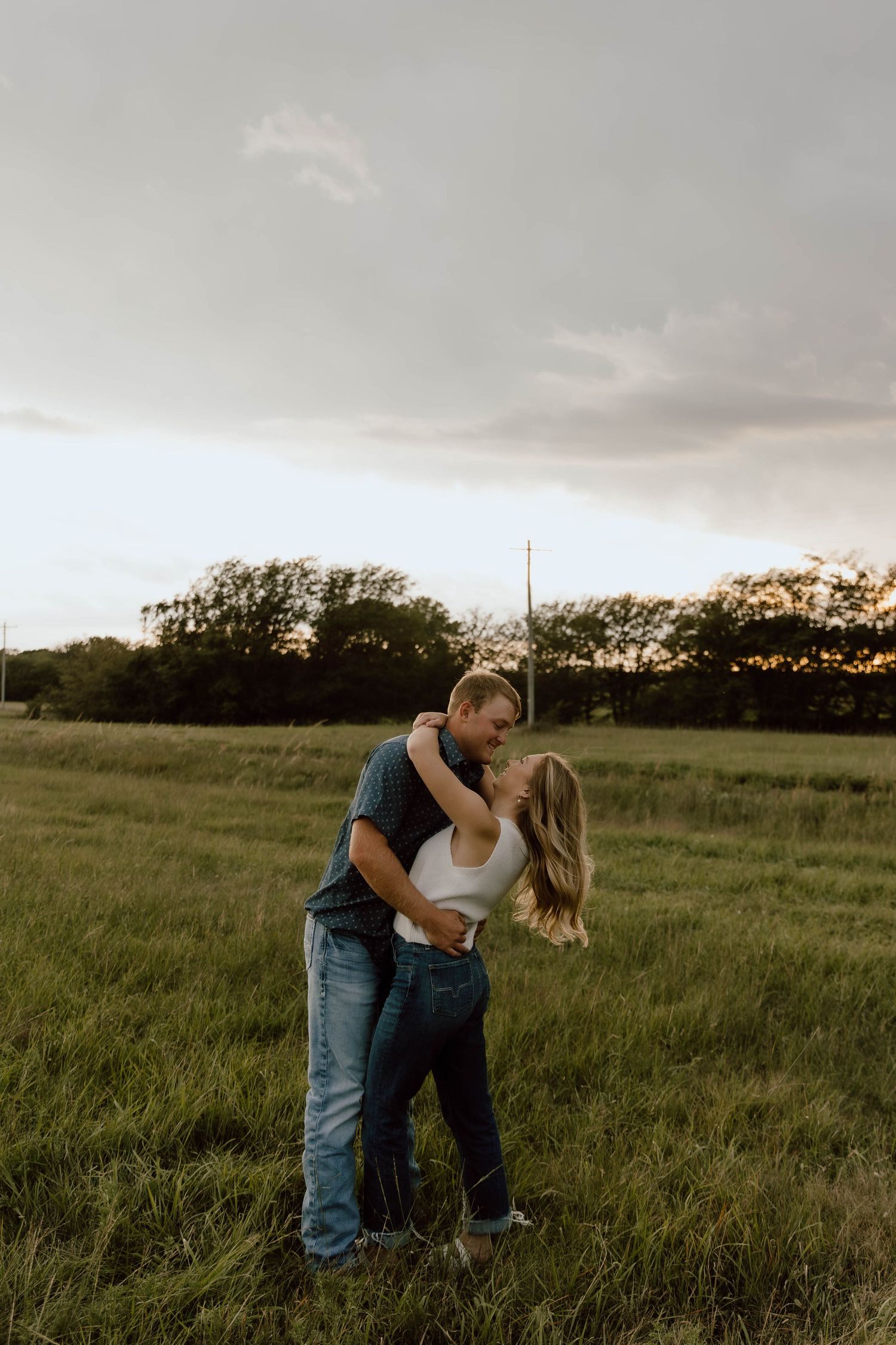 Romantic couple embracing in a grassy field at sunset.