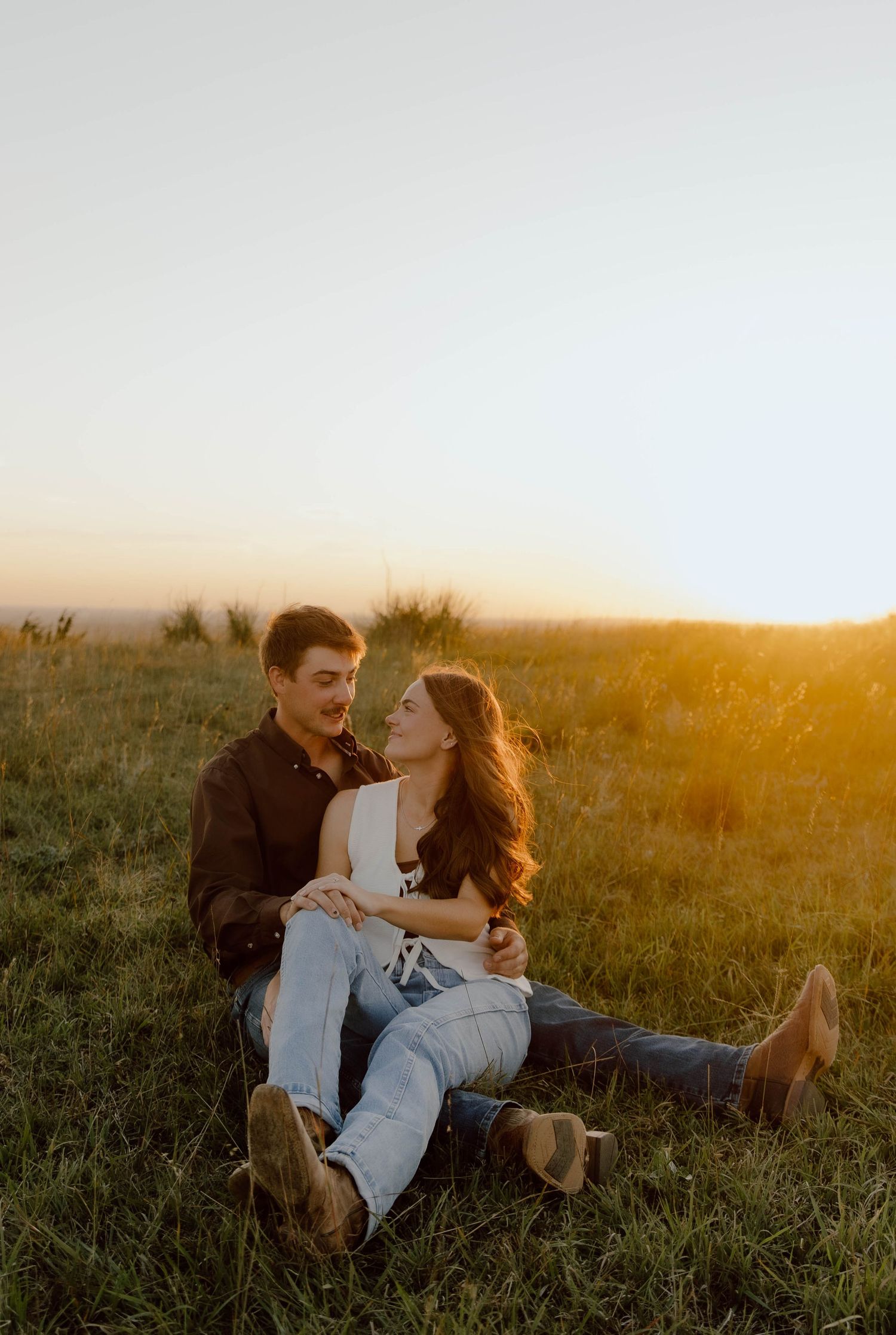 A couple shares an intimate moment in a grassy field at golden hour during sunset.