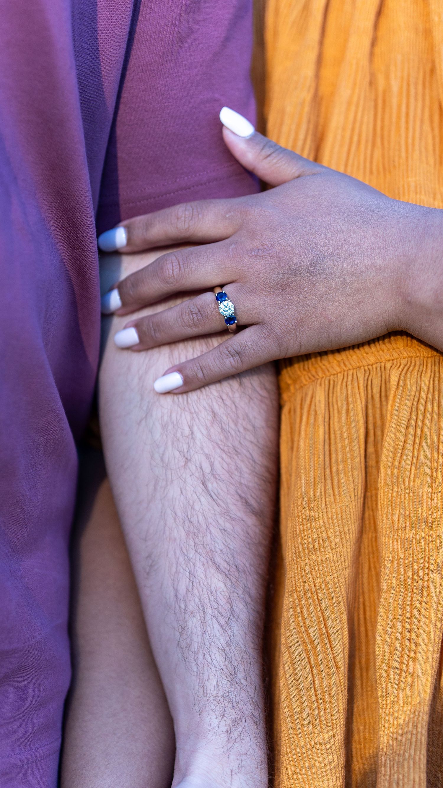 Close-up of an engagement ring with blue sapphires on a woman's hand resting on a man's arm. In Jerusalem mill in Fallston Maryland