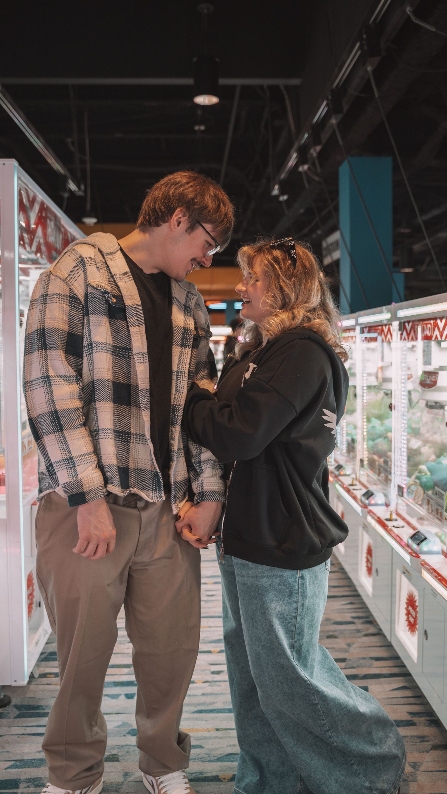 Young couple holding hands and smiling at each other in an arcade game room aisle. In Towson Maryland