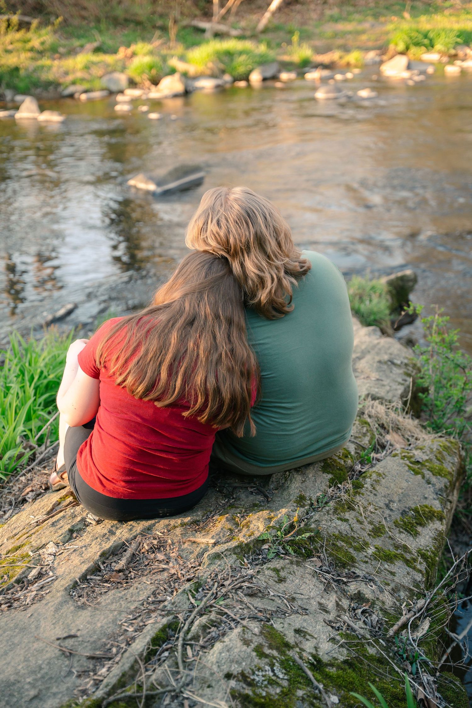 A couple sitting together on a rock by a peaceful stream, one resting her head on the other.  In Jerusalem mill in Fallston Maryland