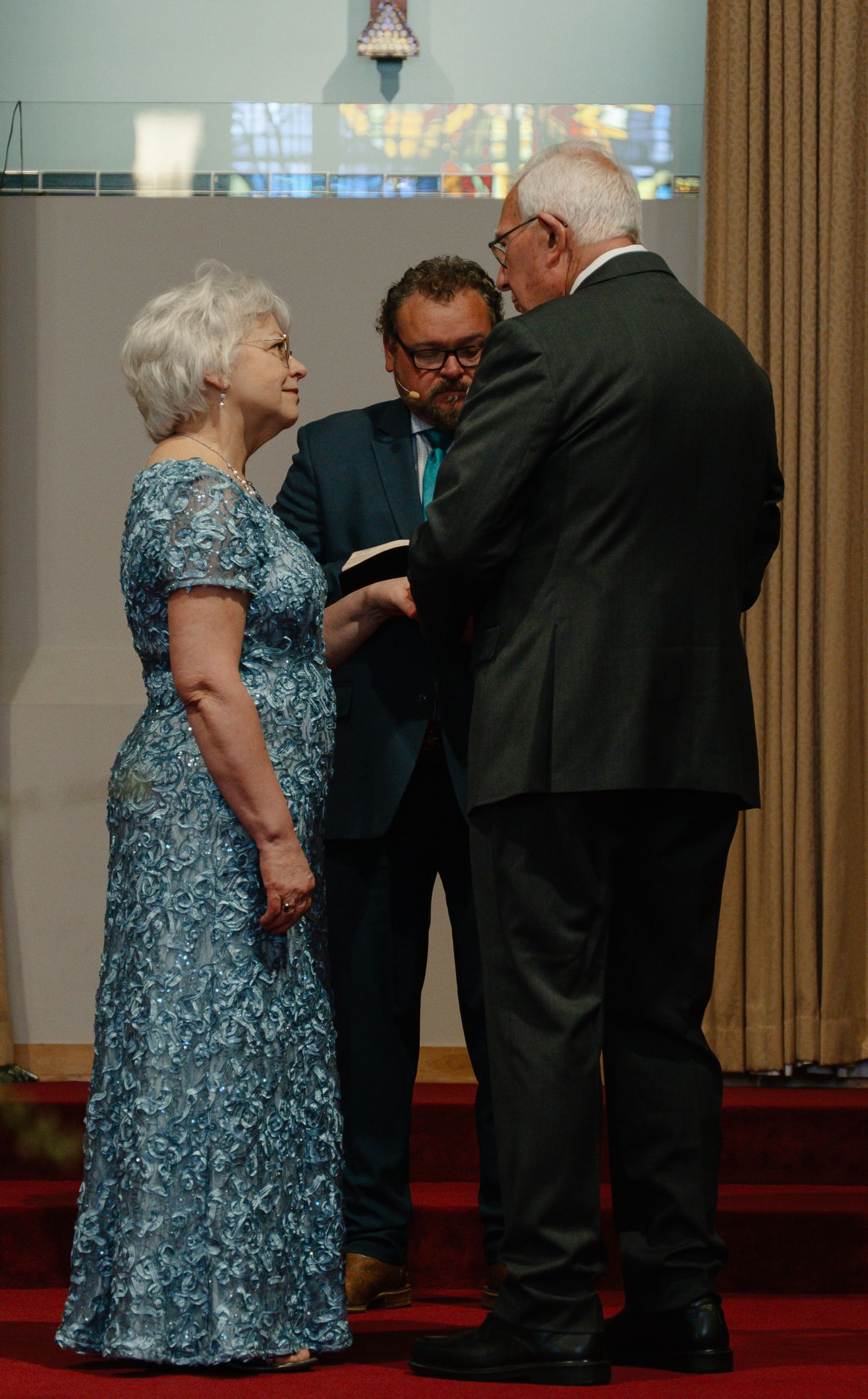 In Bel Air Maryland Elderly couple exchanging vows at a wedding ceremony with an officiant in a church, bride wearing a blue lace gown.
