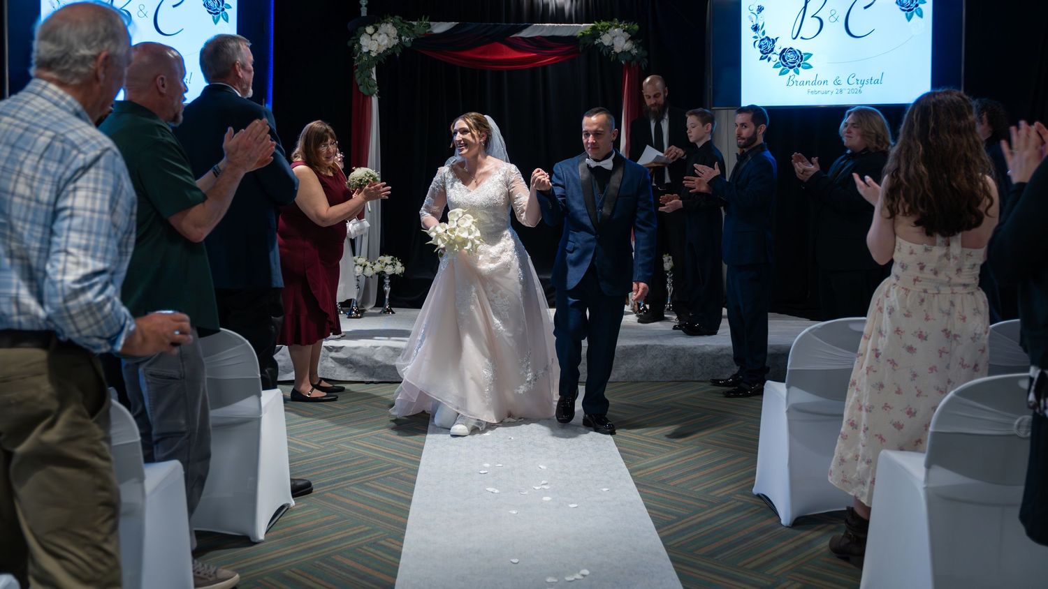 Bride in white lace gown and groom in navy suit walk down aisle while guests celebrate at wedding ceremony.in Abingdon Maryland