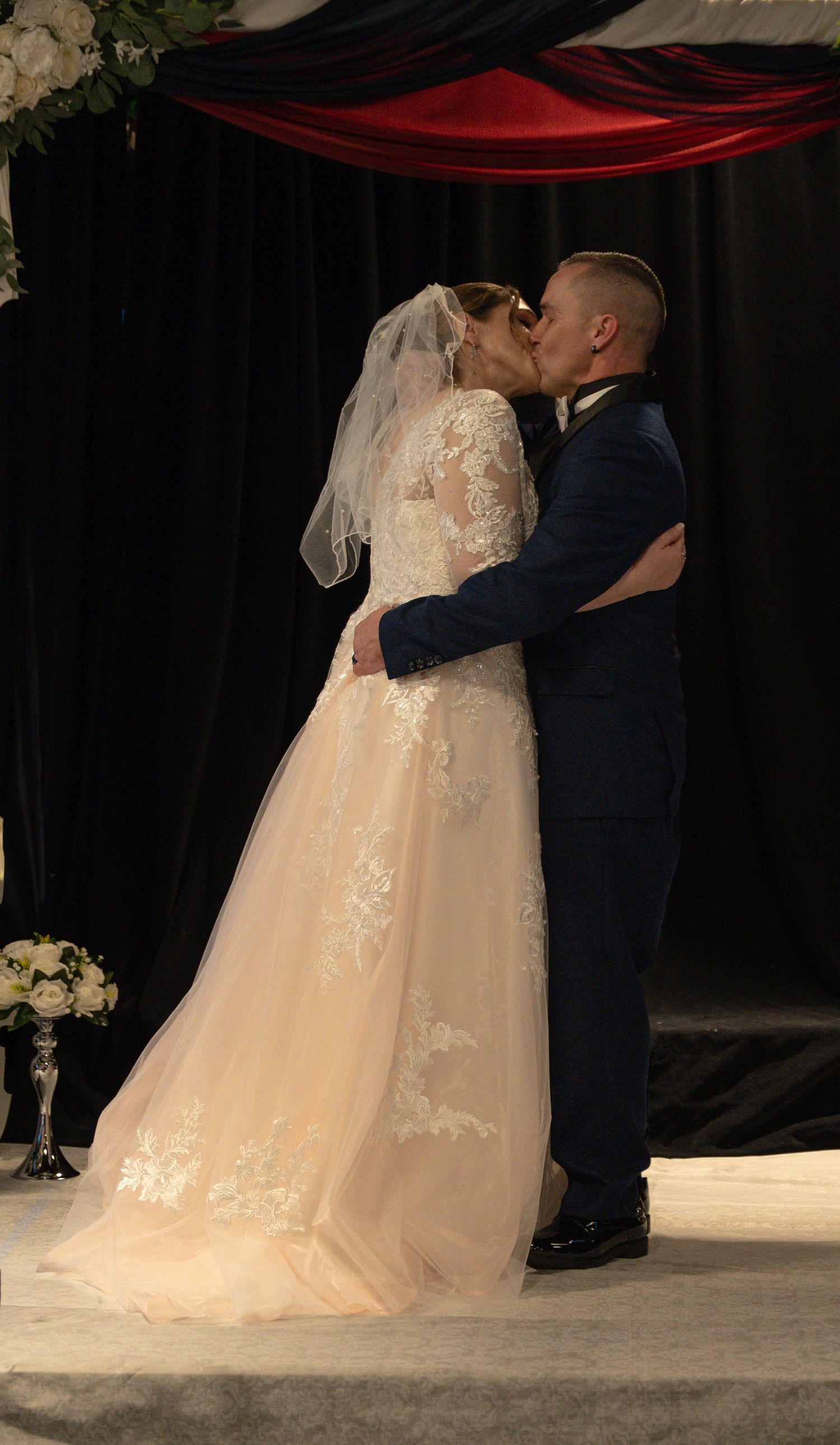 Bride in lace gown and groom in navy suit share first kiss at wedding ceremony altar. In Abingdon Maryland