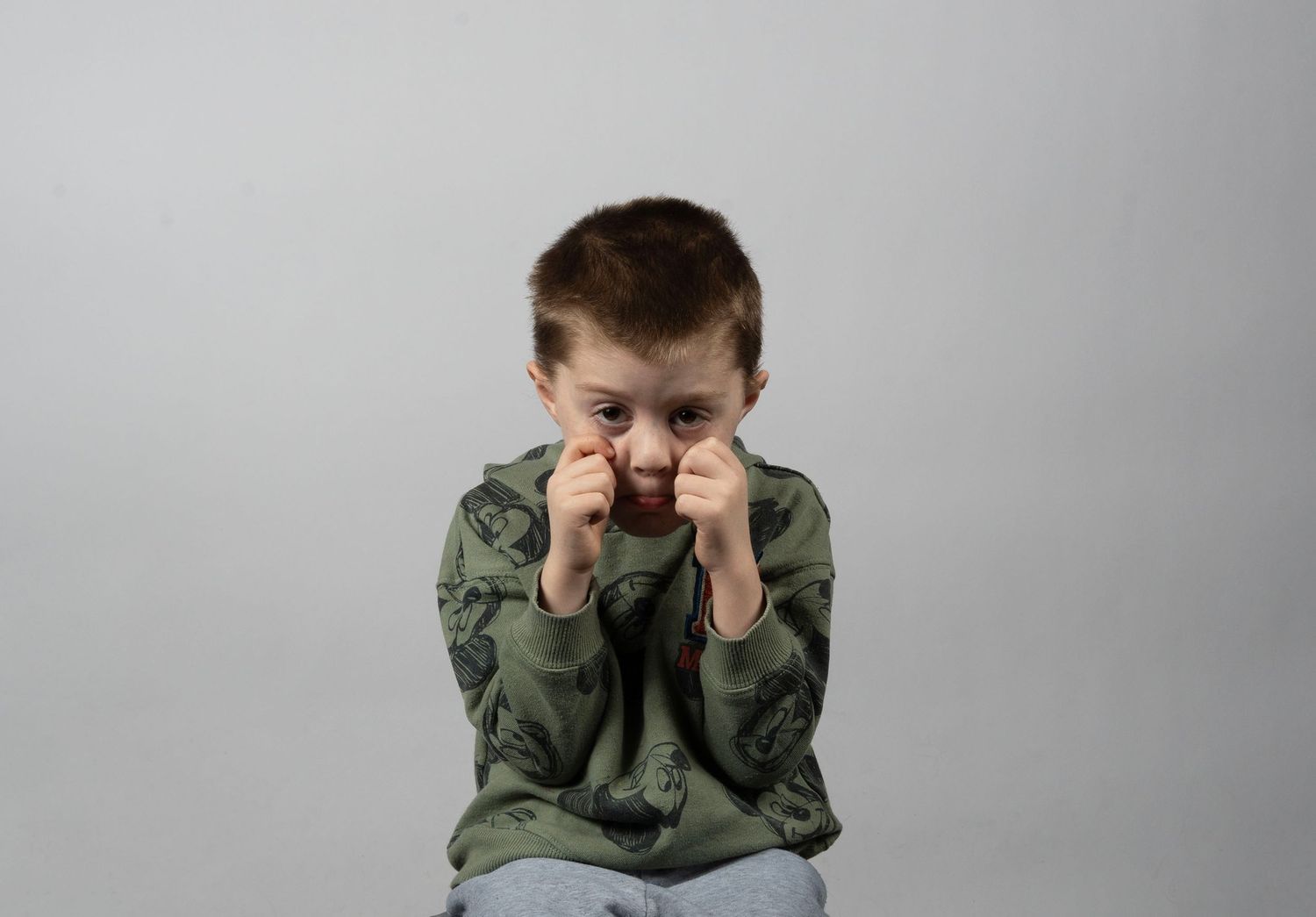 Young boy in green jacket making a fierce face with fists raised, isolated on gray background.