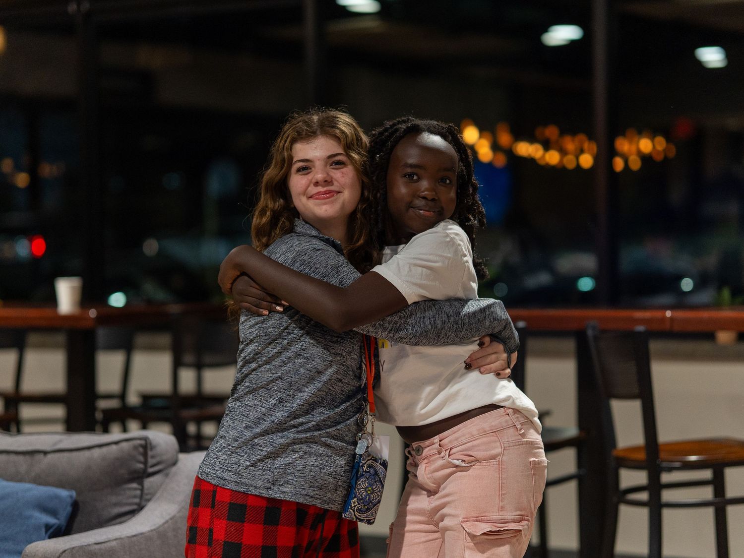 Two young women share a warm embrace while smiling inside a dimly lit indoor venue at night. In Abingdon Maryland