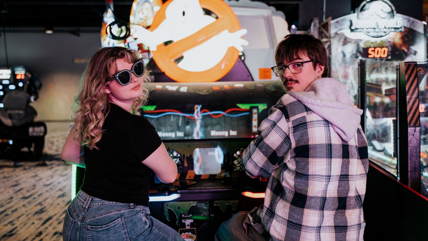 A young couple strikes a cool pose in front of a Ghostbusters arcade game wearing sunglasses. In Towson Maryland