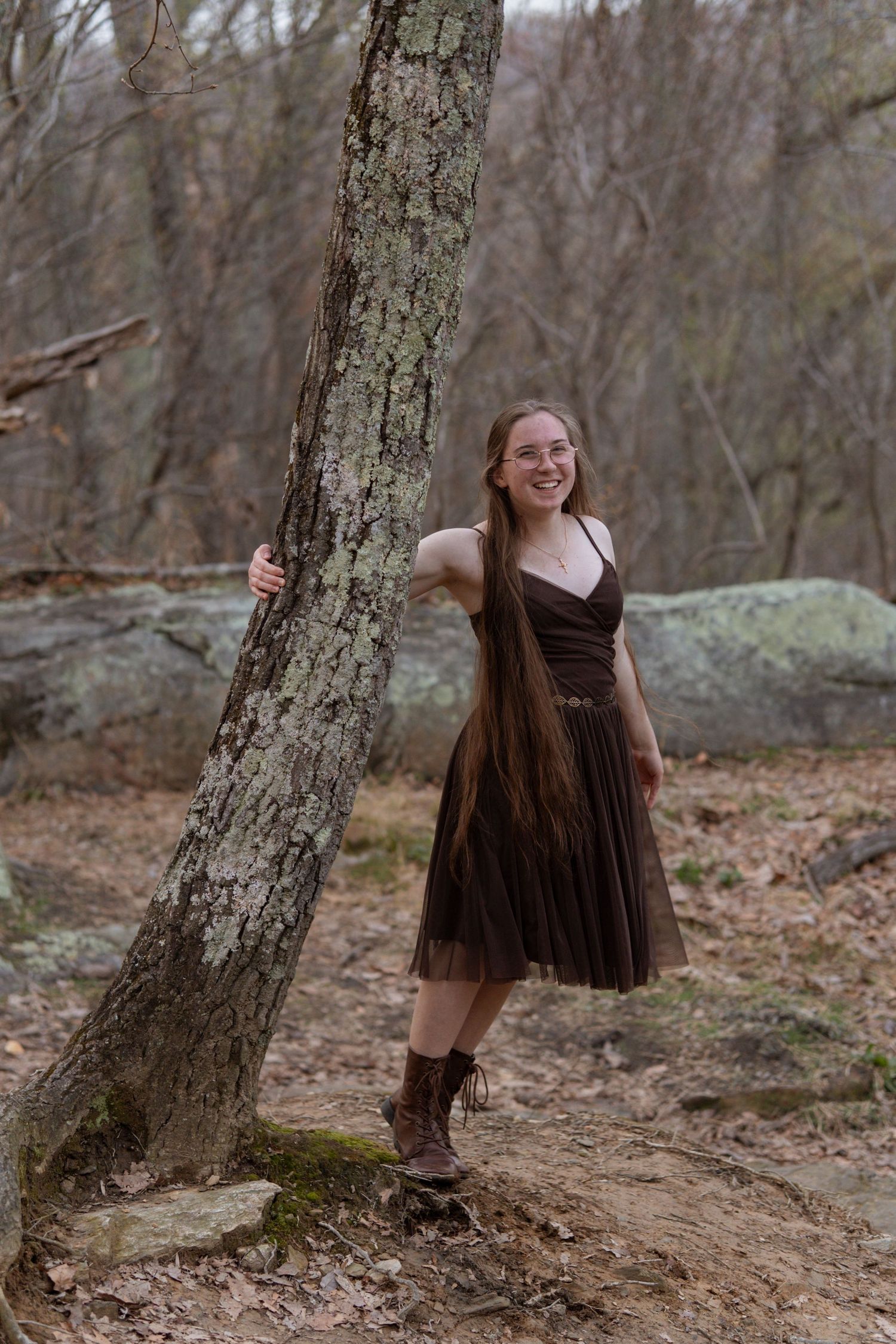 Young woman in brown dress leaning against tree trunk in wooded forest setting. in Maryland Rock state park Senior