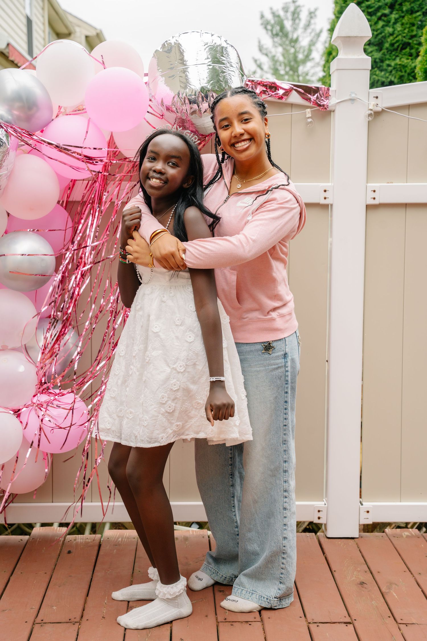 Two girls posing together outdoors at a birthday party with pink and silver balloons and tinsel decorations. In Bel Air Maryland