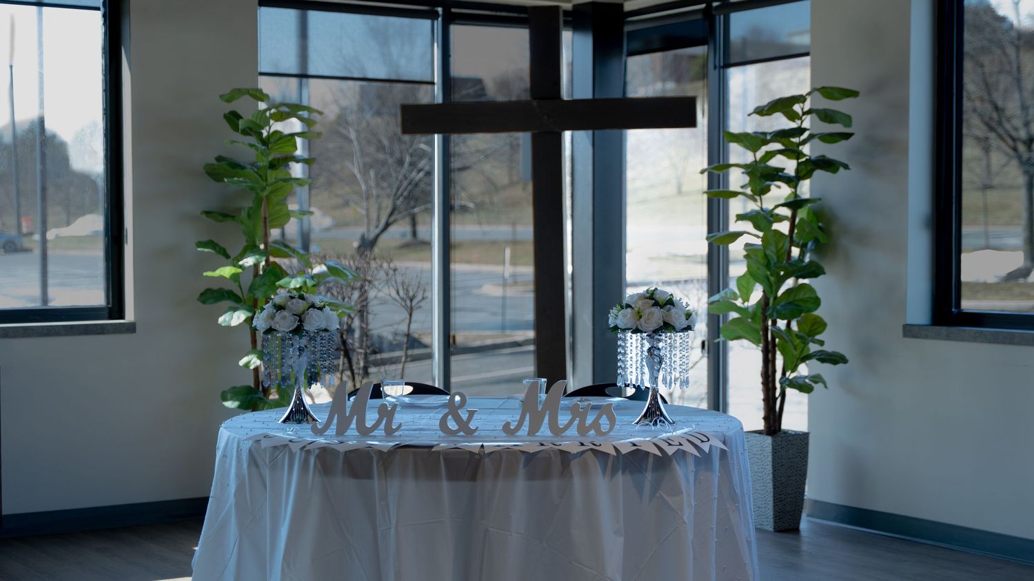 An elegant wedding sweetheart table draped in blue linen with floral arrangements sits before large cross-shaped windows. In Abingdon MD
