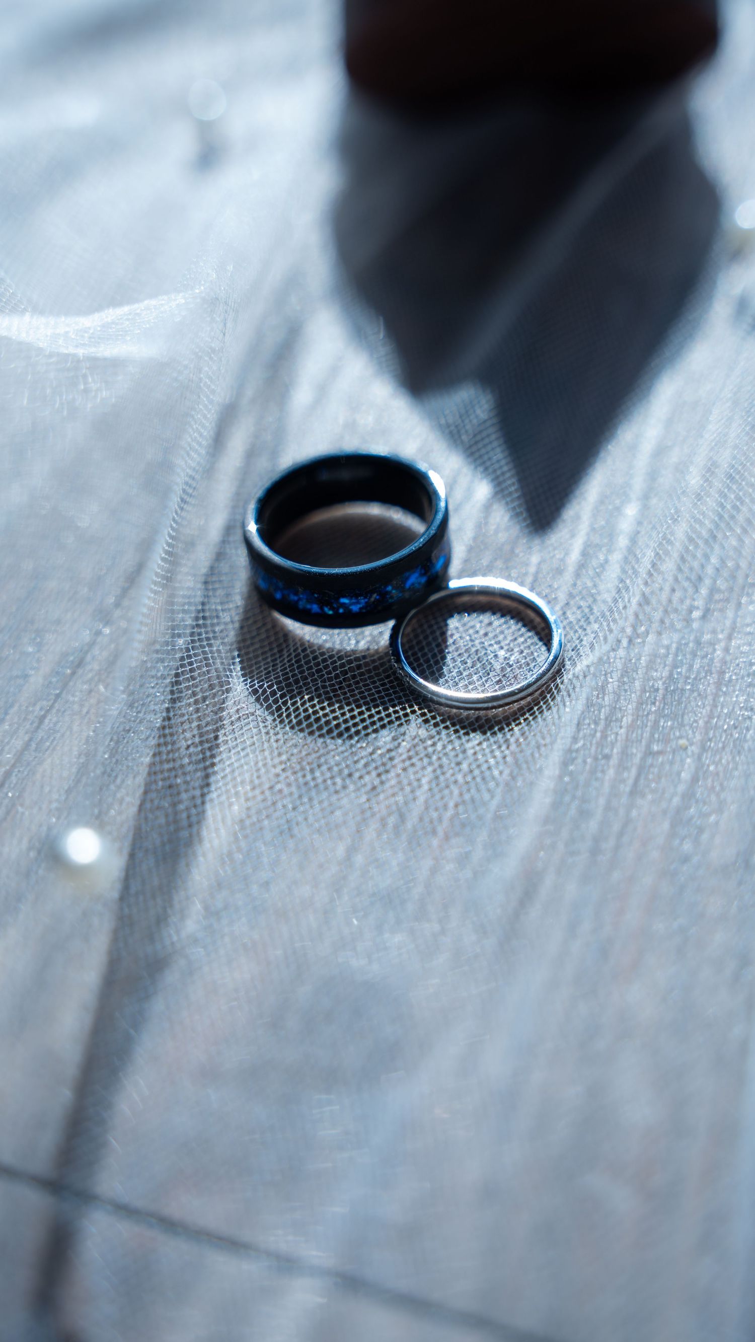 Blue patterned groom ring and silver bride wedding band resting on delicate white tulle fabric. in Abingdon Maryland