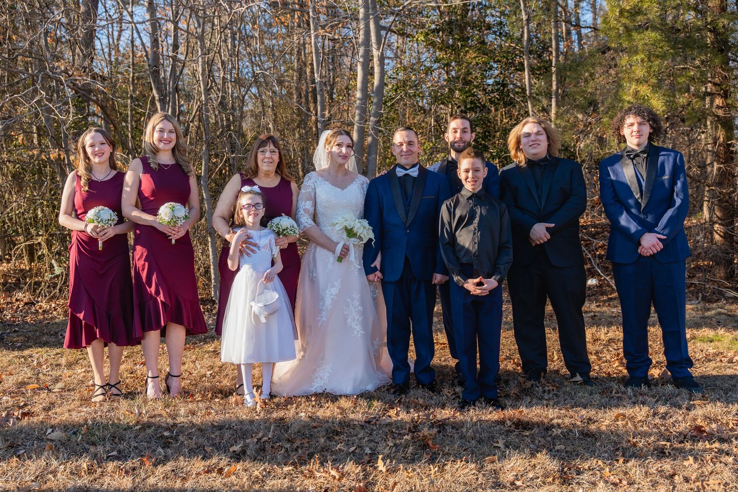 Wedding party poses outdoors in autumn, bridesmaids in burgundy dresses and groomsmen in navy suits with bride and groom.in Abingdon Marylan