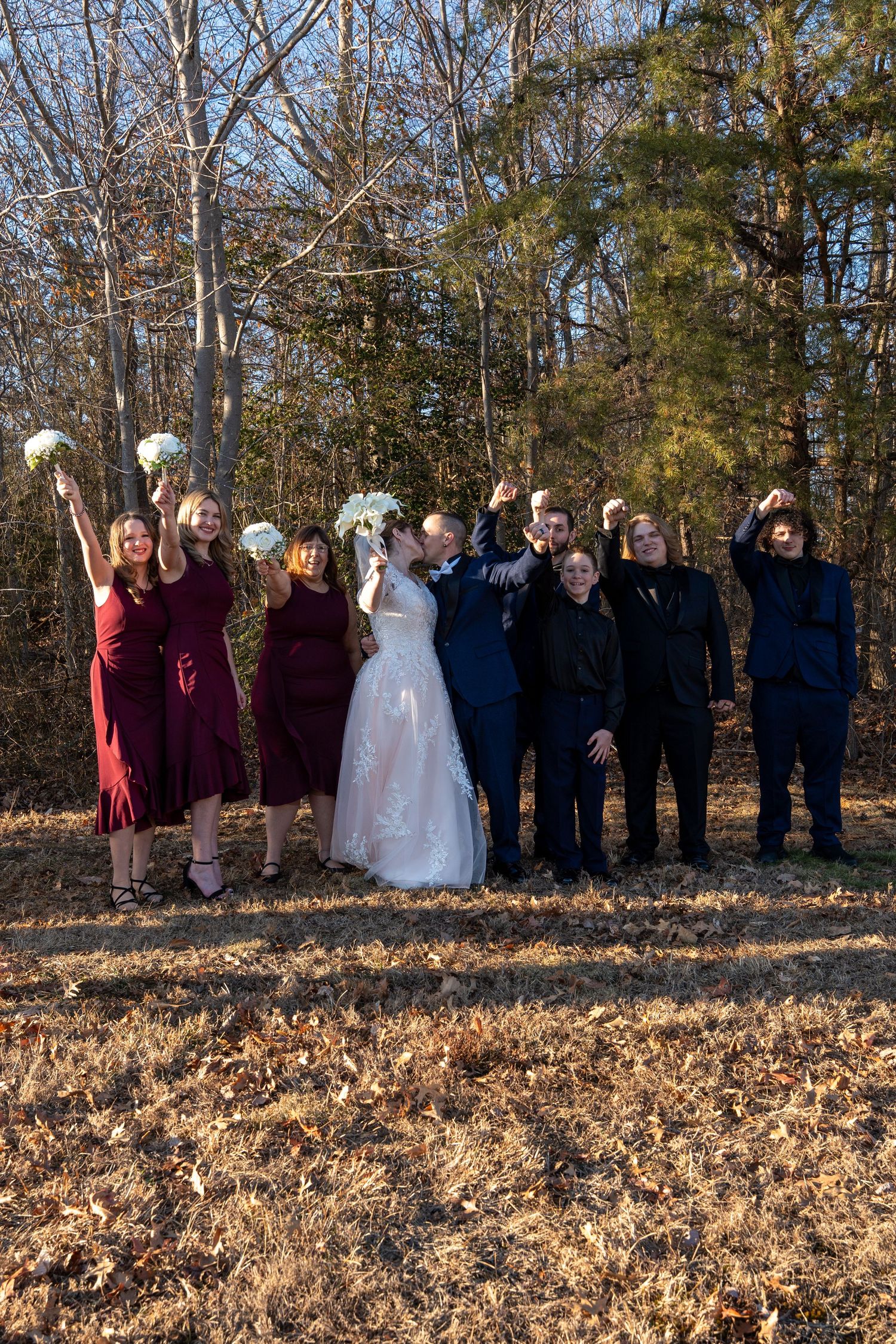 Wedding party celebrates outdoors in autumn woods with bride in white gown and attendants in burgundy dresses.in Abingdon Maryland