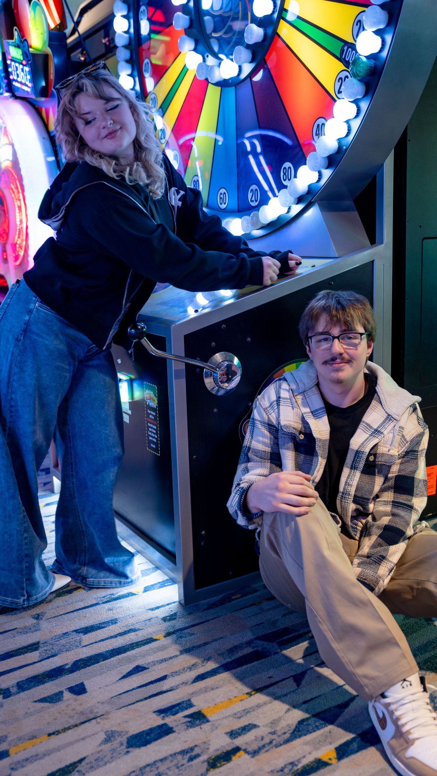 A young couple poses playfully at a colorful arcade game machine with bright neon lights. In Towson Maryland