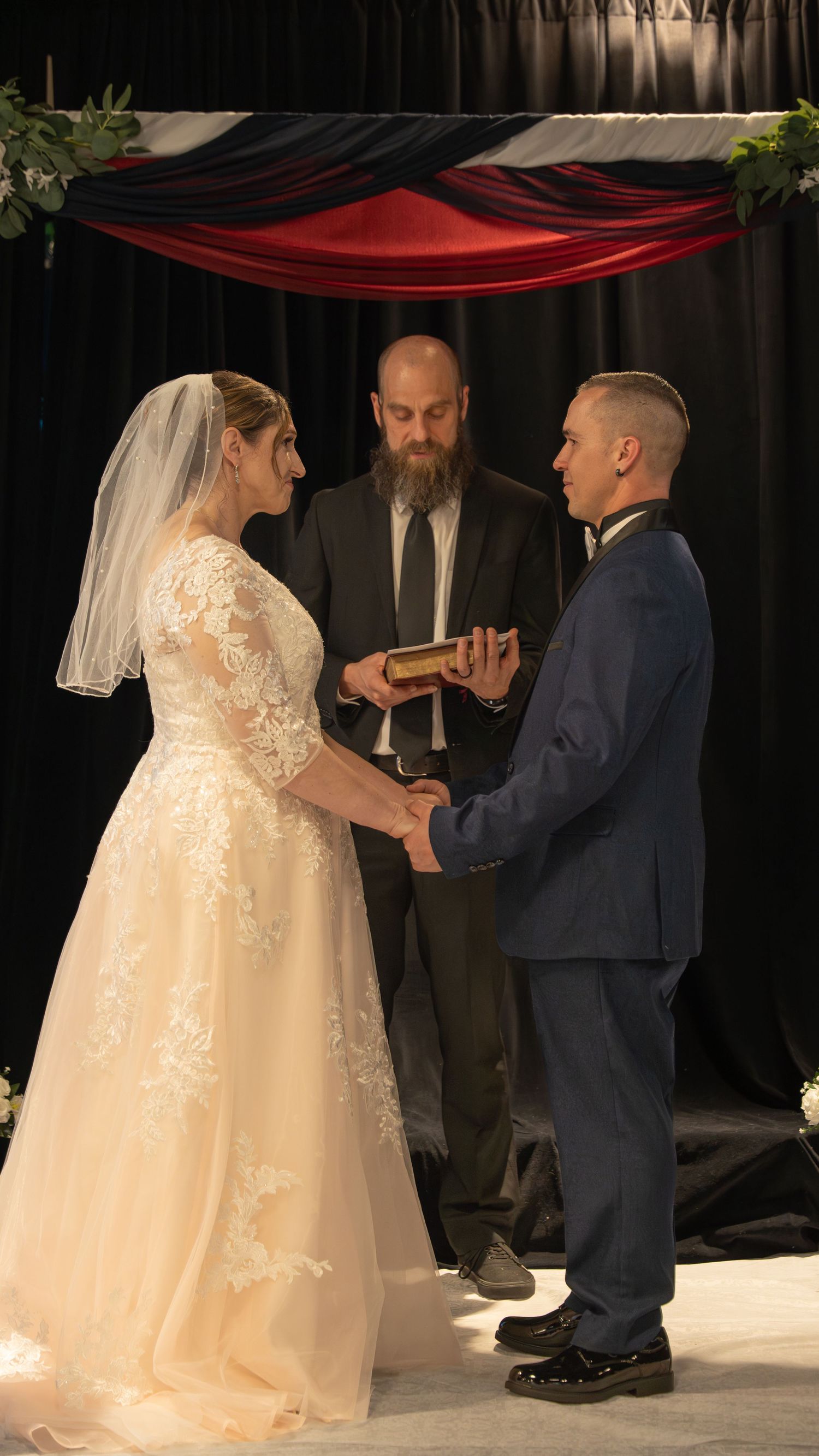 Bride and groom exchange vows holding hands before a bearded officiant at an elegant wedding ceremony. In Abingdon Maryland
