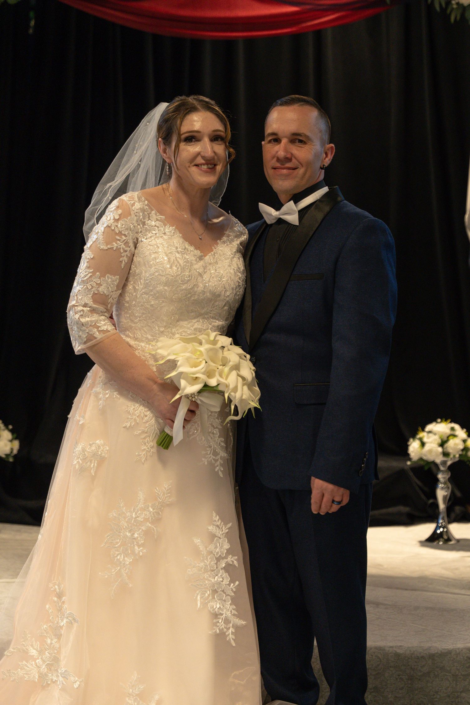 Bride in lace wedding gown holding white bouquet stands with groom in navy suit at wedding ceremony altar. Abingdon Maryland
