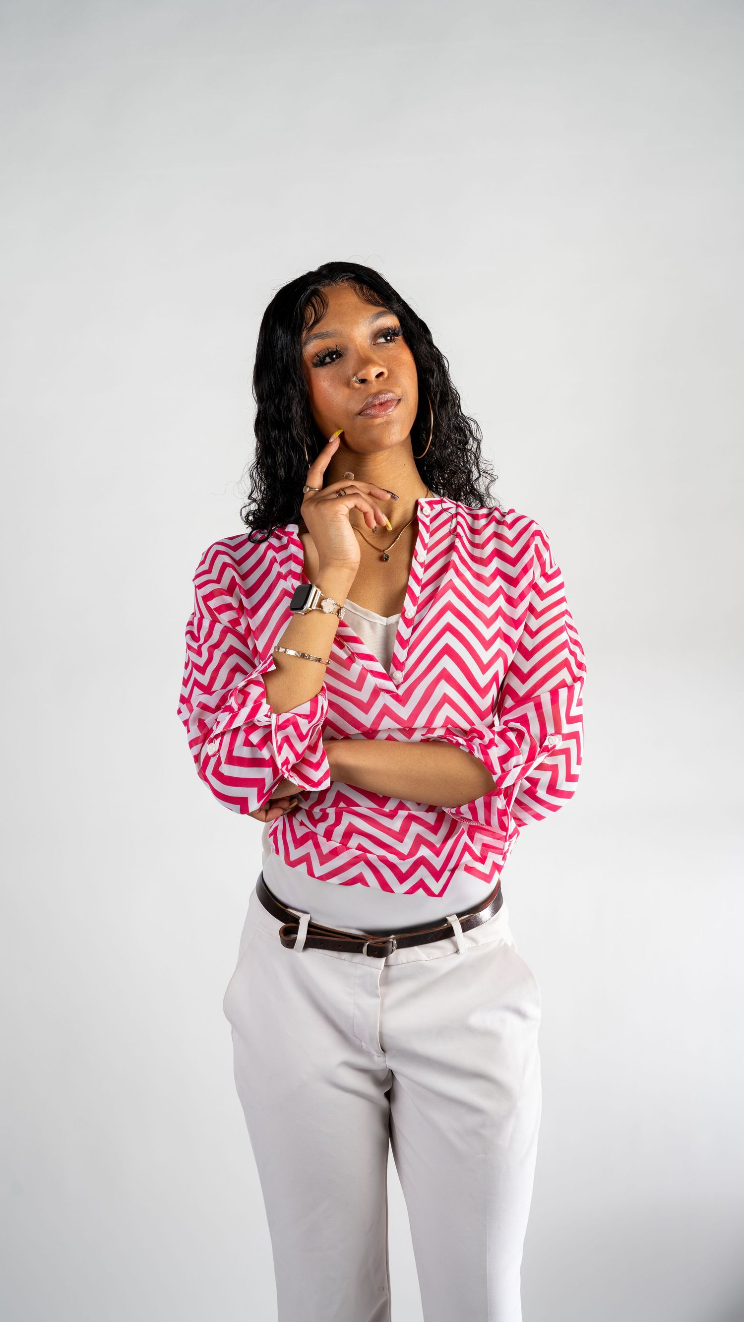 Stylish woman in pink and white chevron blazer standing confidently with arms crossed in a white studio.In Bel Air Maryland