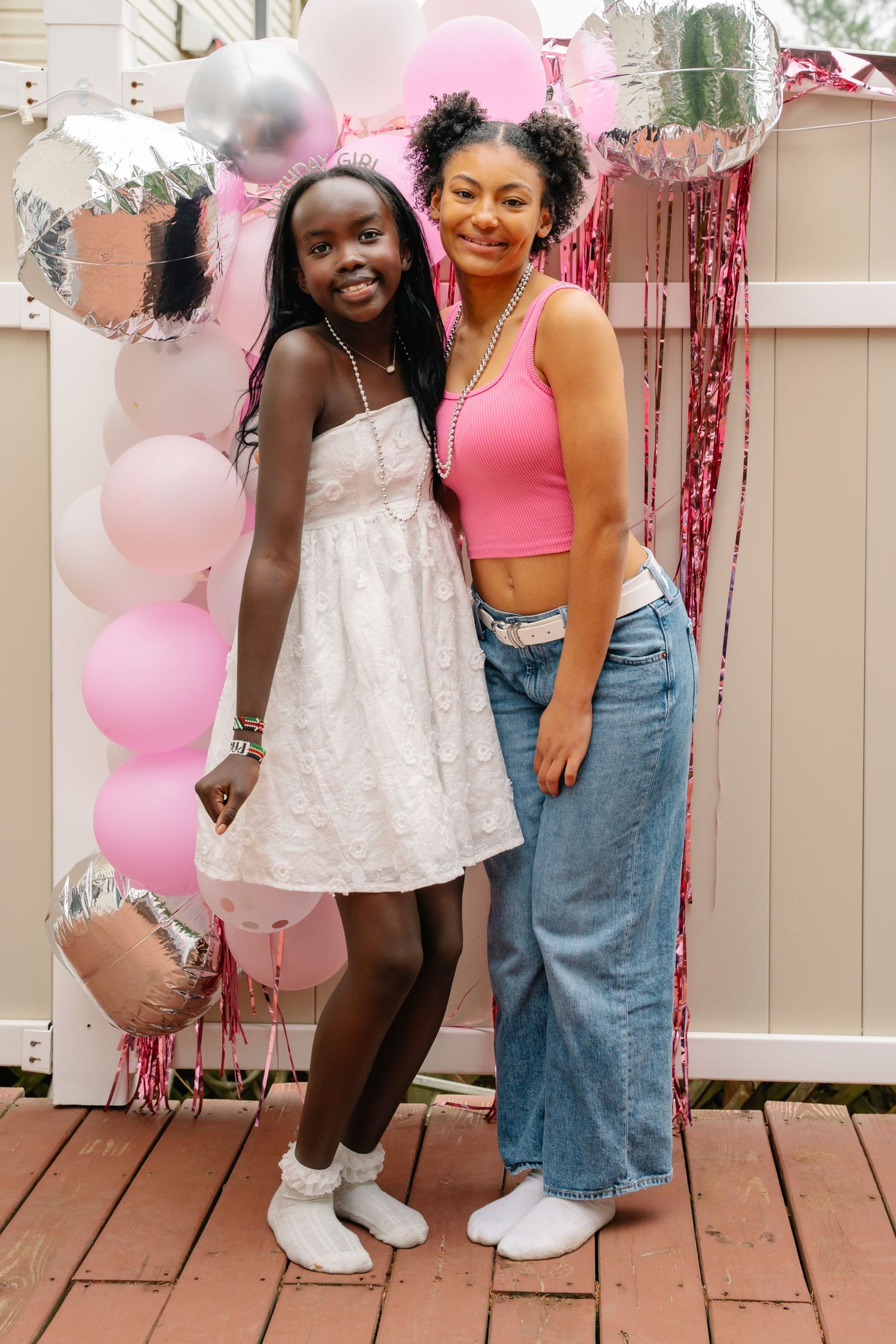 bel air maryland Two girls pose together at a pink balloon party backdrop, one in white dress, other in pink crop top and jeans.