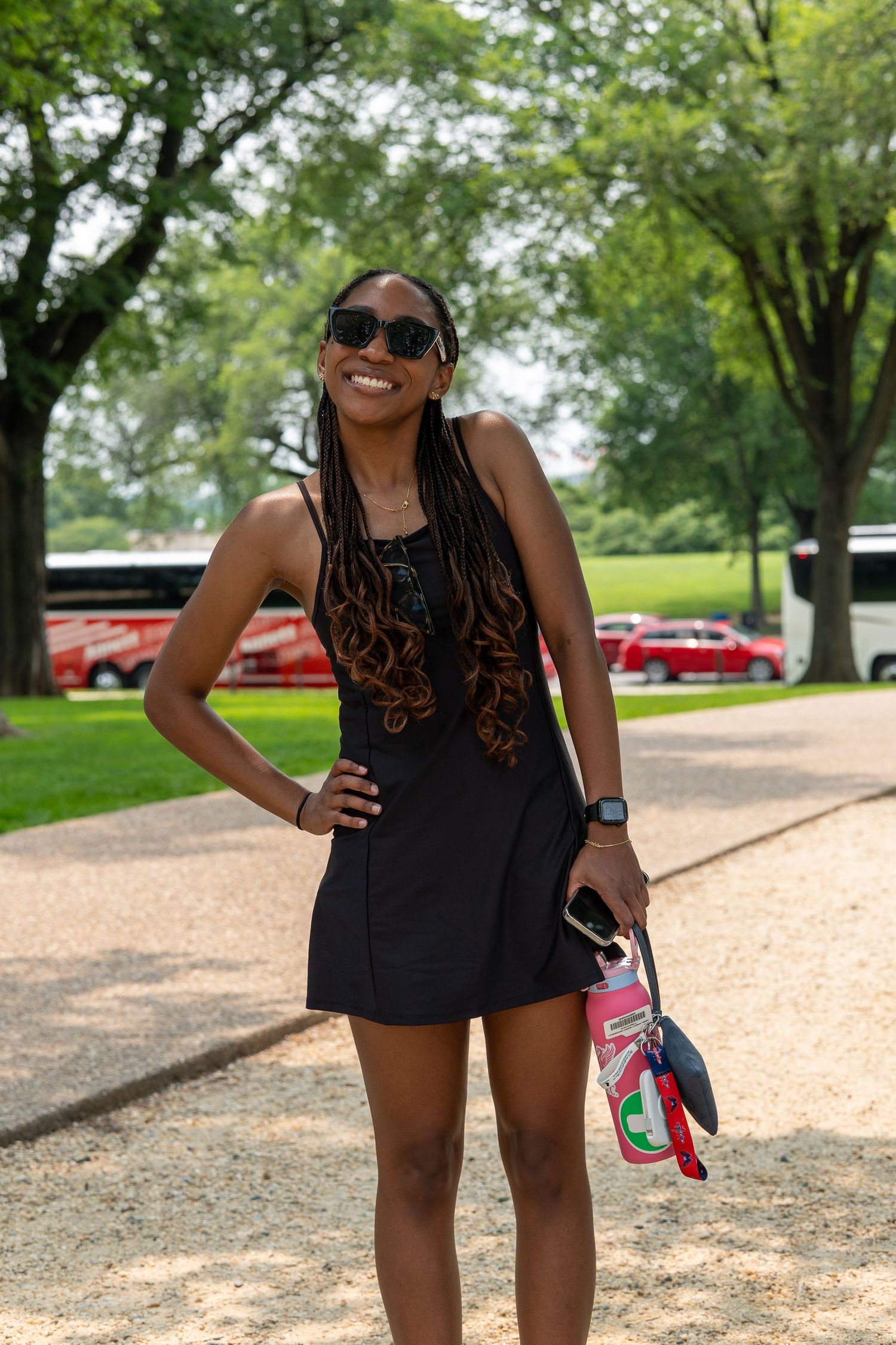 Smiling woman in black dress and sunglasses holding a colorful bag, posing outdoors on a sunny day. In Washington DC