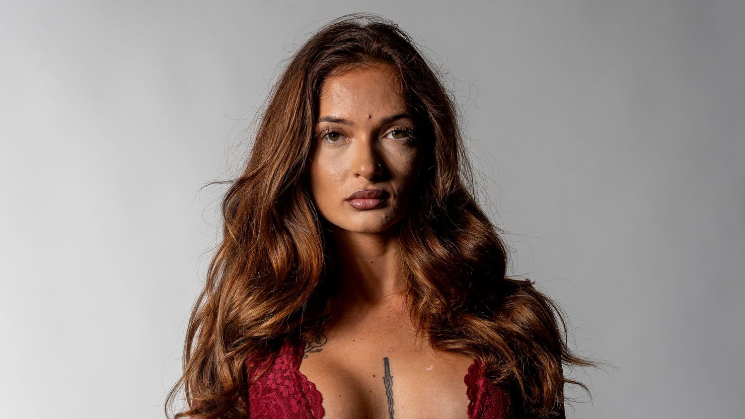 A woman with long brunette hair wearing a red lace top poses against a light gray background.In Bel Air Maryland