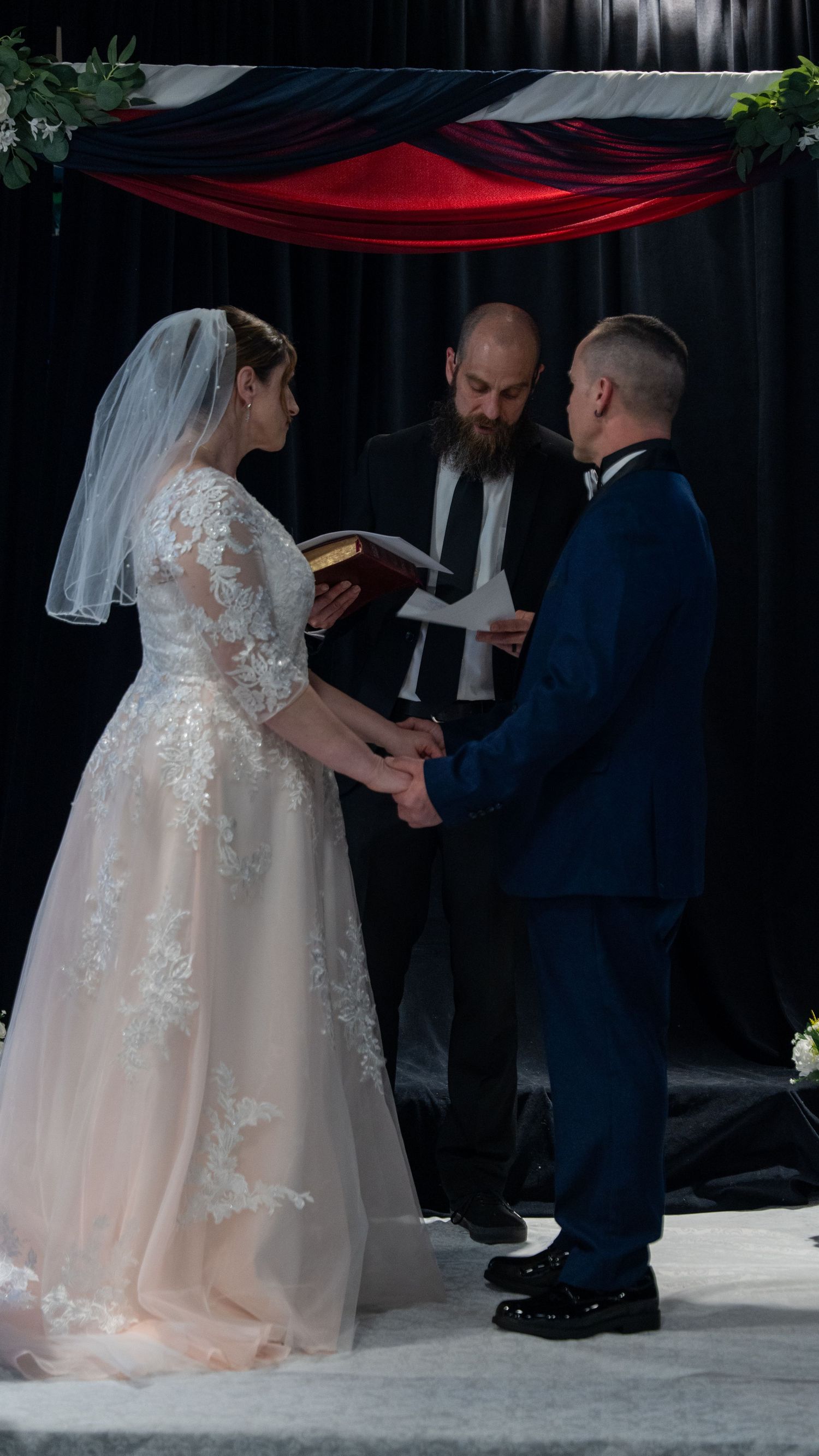 Bride and groom exchange vows holding hands before bearded officiant at decorated wedding altar. in Abingdon, Maryland