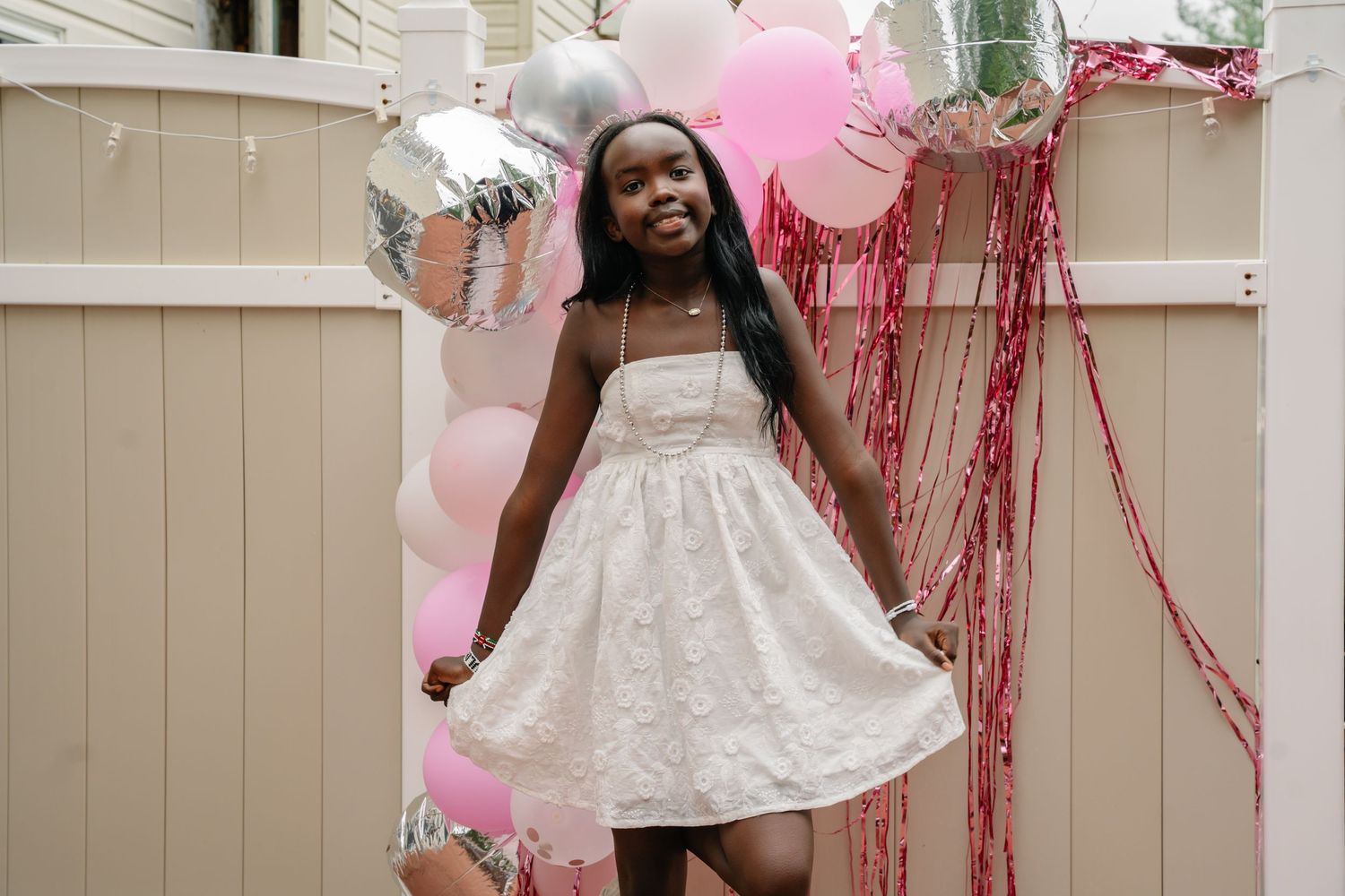 Bel Air Maryland Young girl in white dress posing happily among pink and silver balloons at a festive outdoor celebration.
