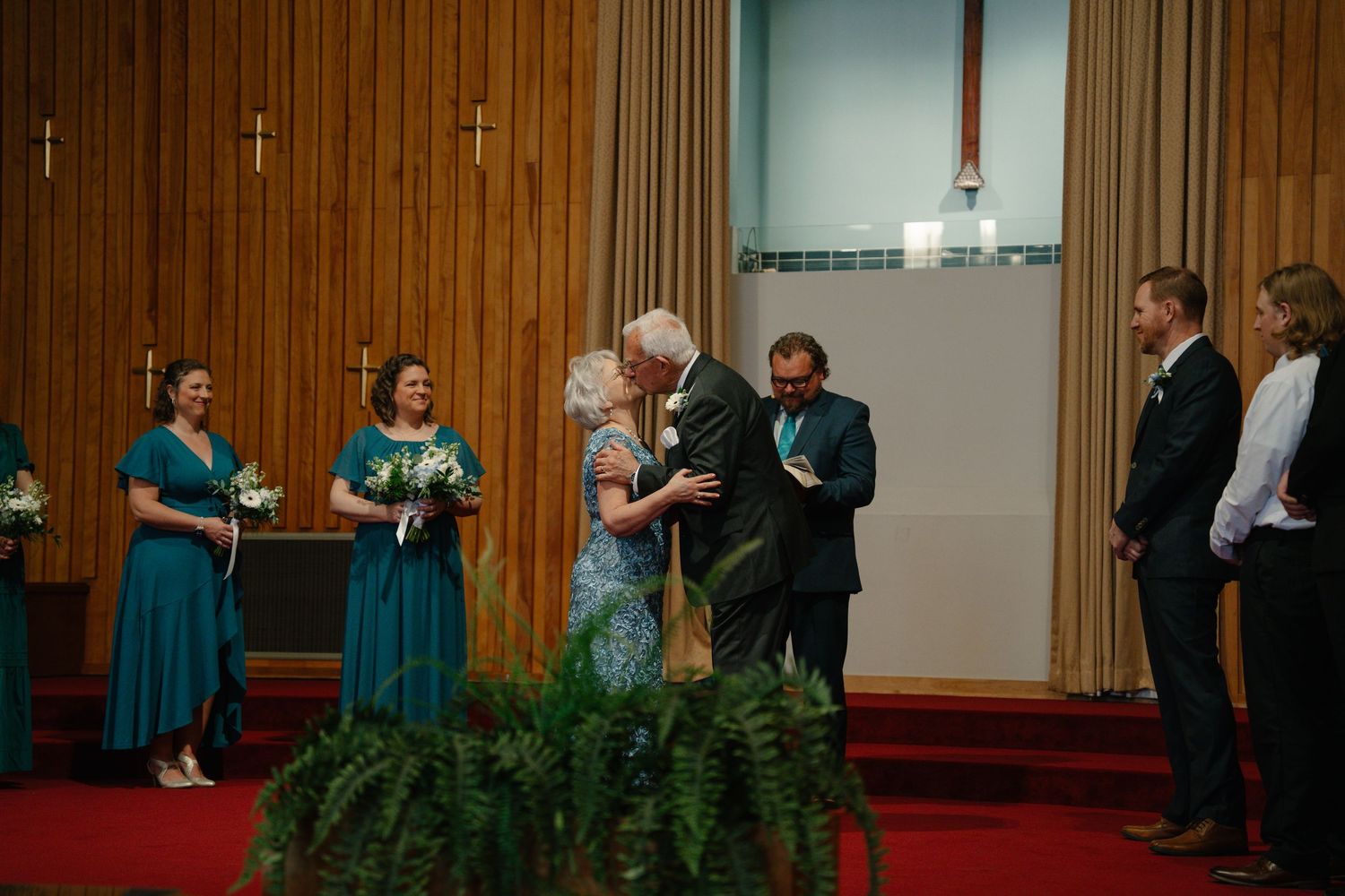 in Bel air Maryland Couple embracing at wedding ceremony altar in church with bridesmaids in teal dresses and guests standing nearby.