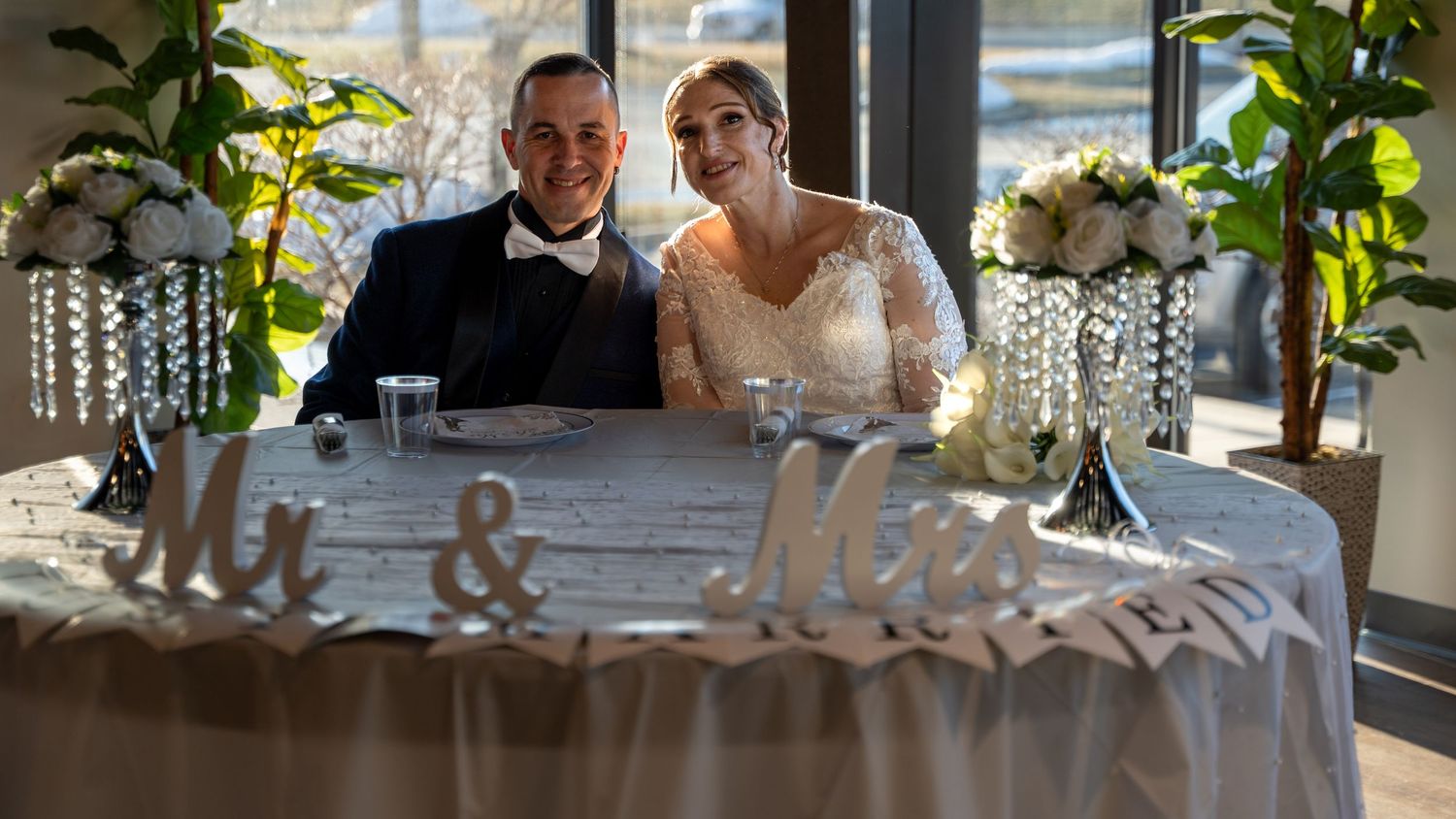 Newlyweds smile together at decorated Mr. and Mrs. sweetheart table with crystal centerpieces at wedding reception. Abingdon Maryland
