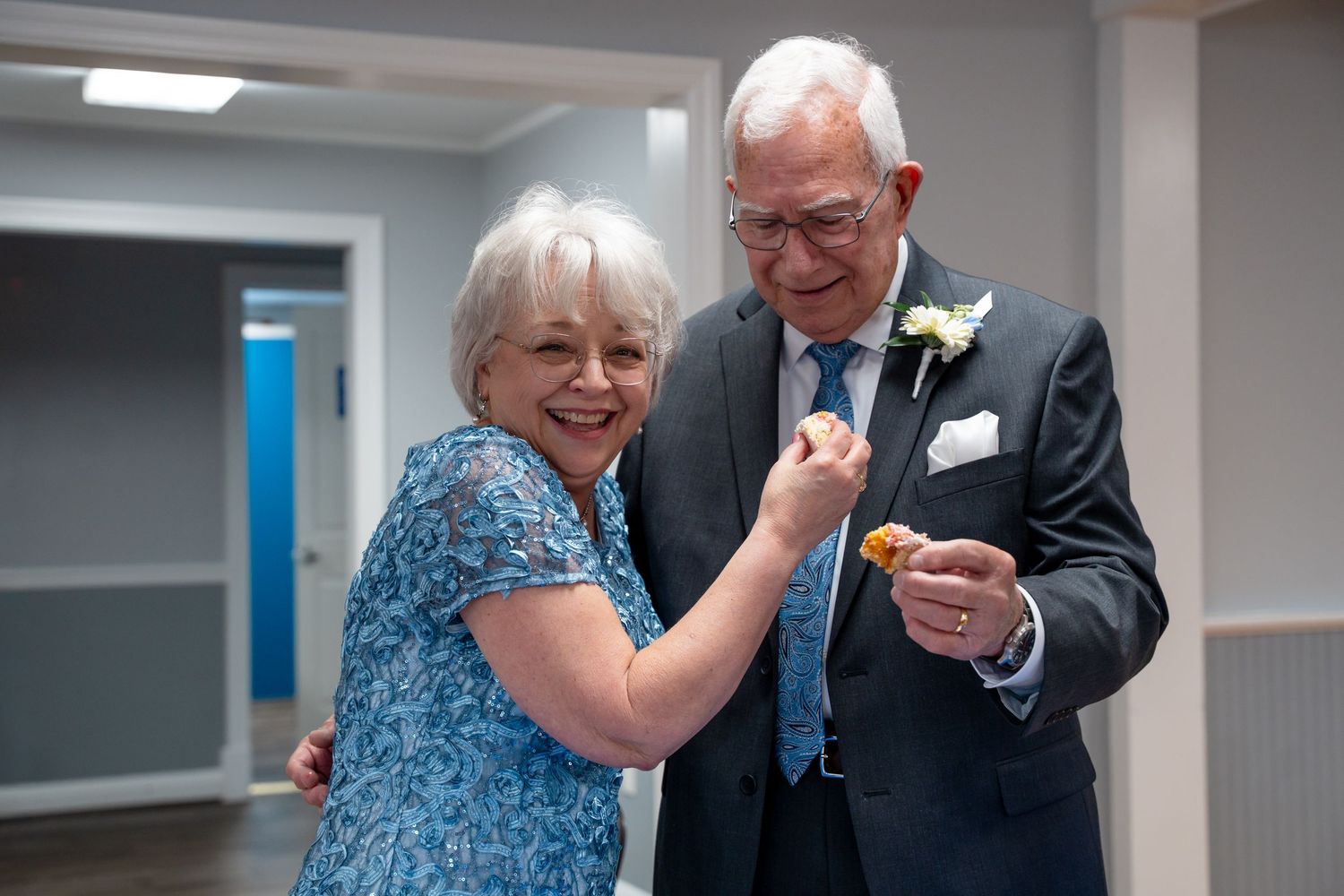 Elderly couple sharing a joyful moment at a wedding, man in navy suit with boutonniere, woman in blue floral dress. In Bel Air Maryland