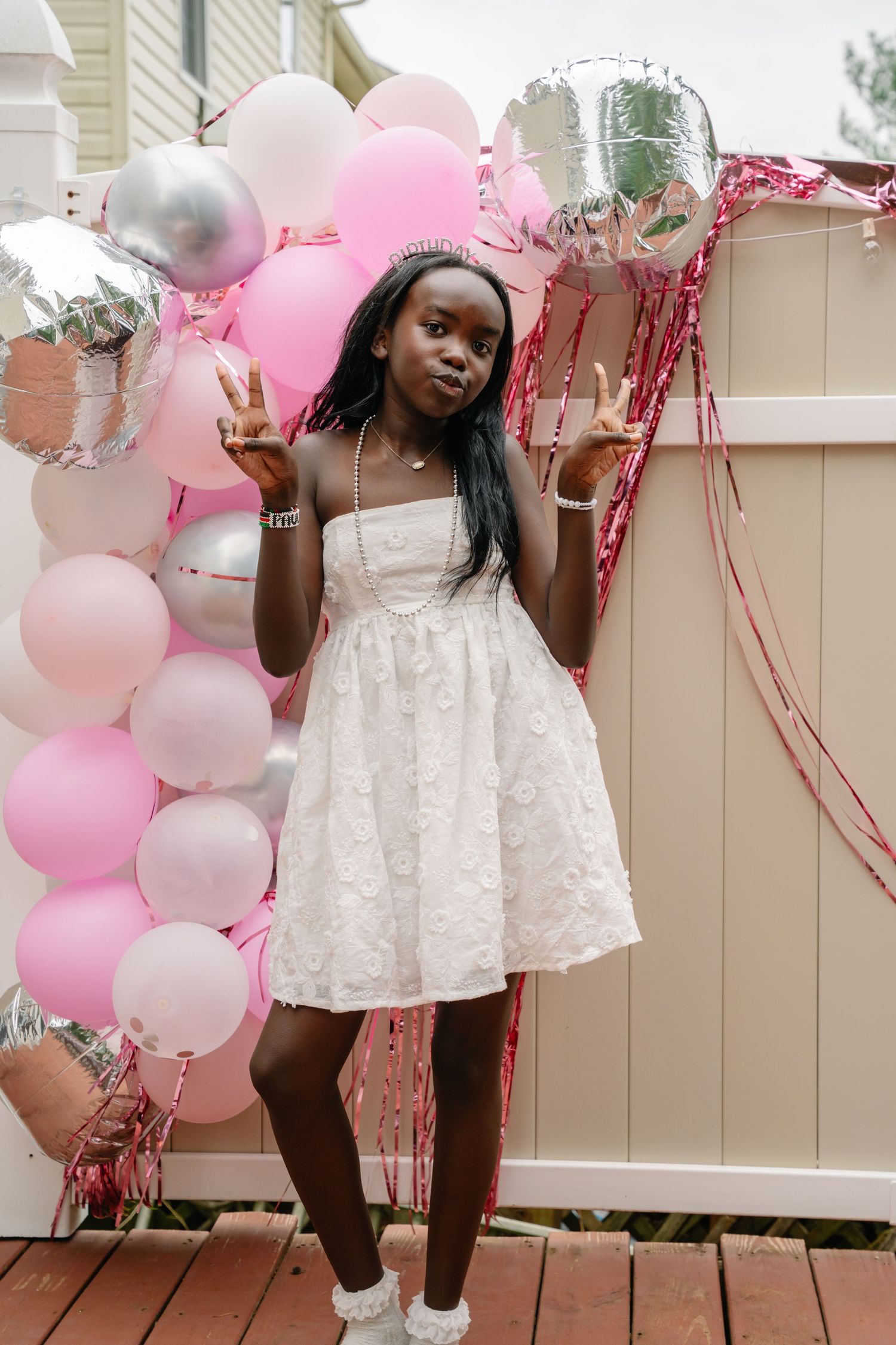 Bel air maryland Young girl in white dress making peace signs in front of pink and silver balloon decoration at a birthday party.