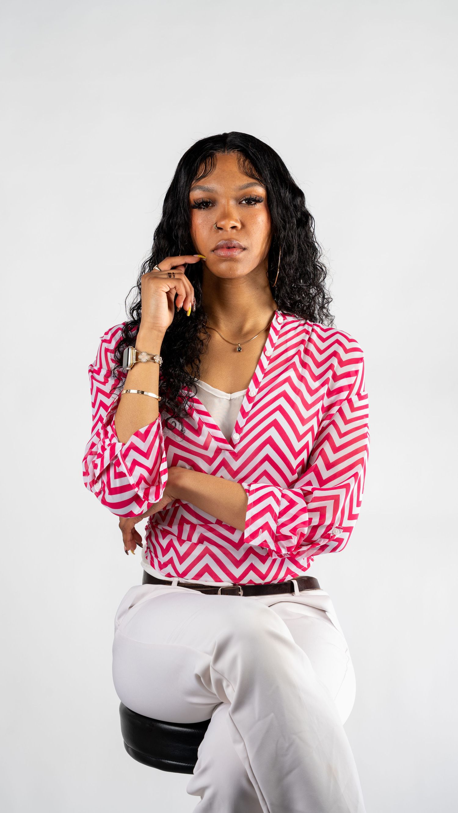 Woman in bold pink zigzag patterned blazer seated, posing thoughtfully with hand on chin in white studio.In Bel Air Maryland