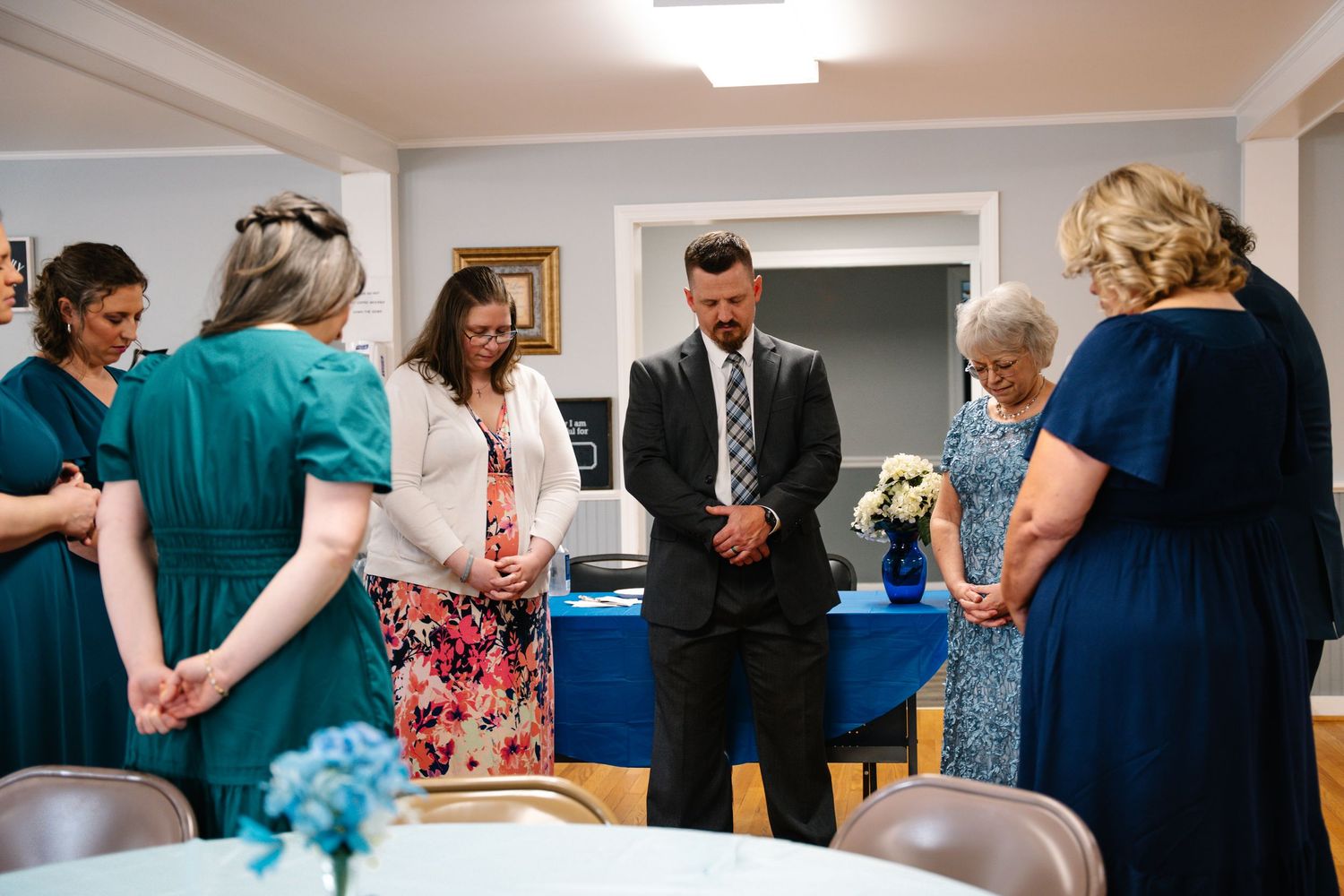In Bel Air Maryland Group of people bowing heads in prayer at a formal gathering around a table with blue tablecloth.