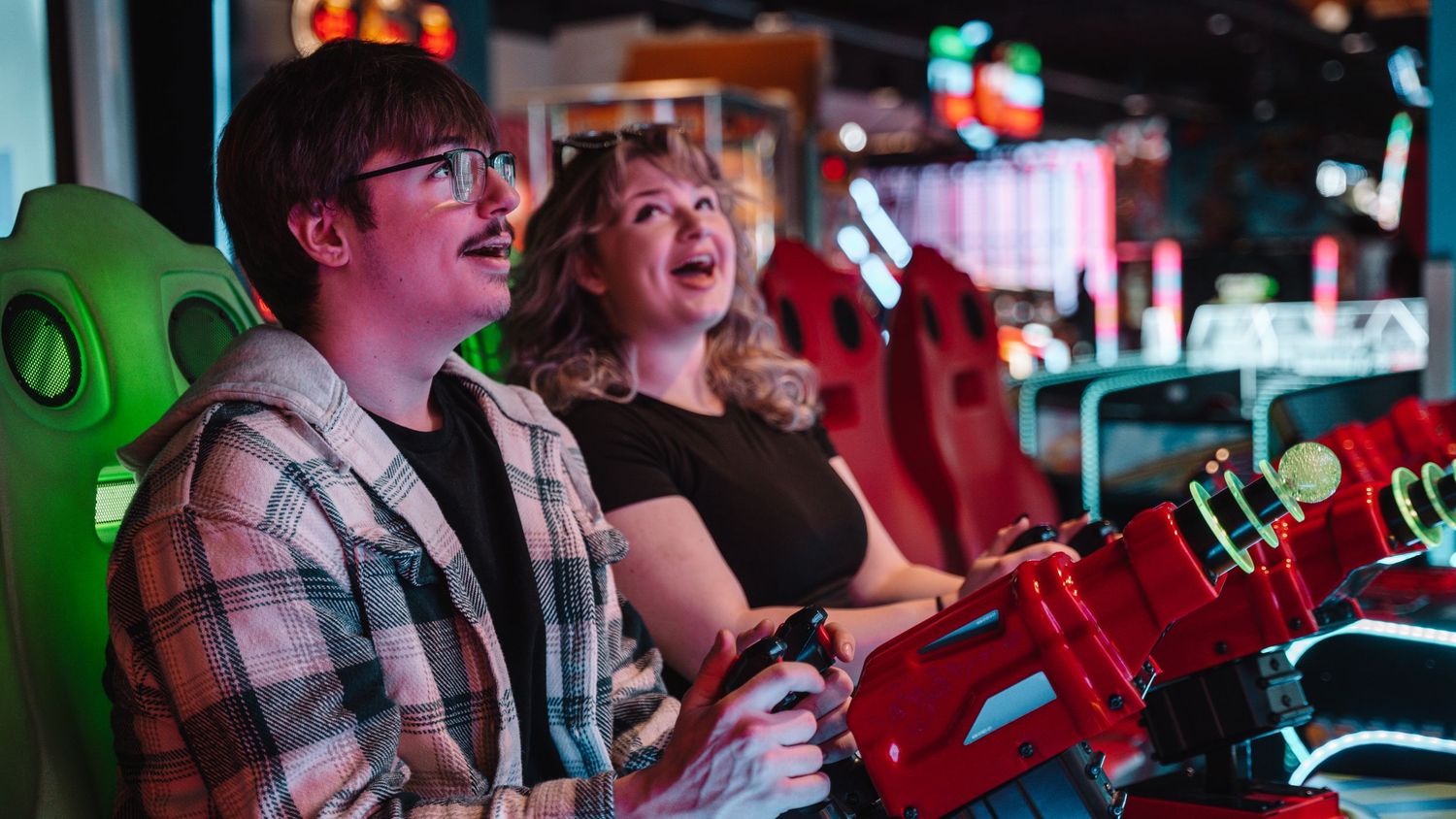 Young couple smiling and playing a racing video game together at an arcade. In Towson Maryland