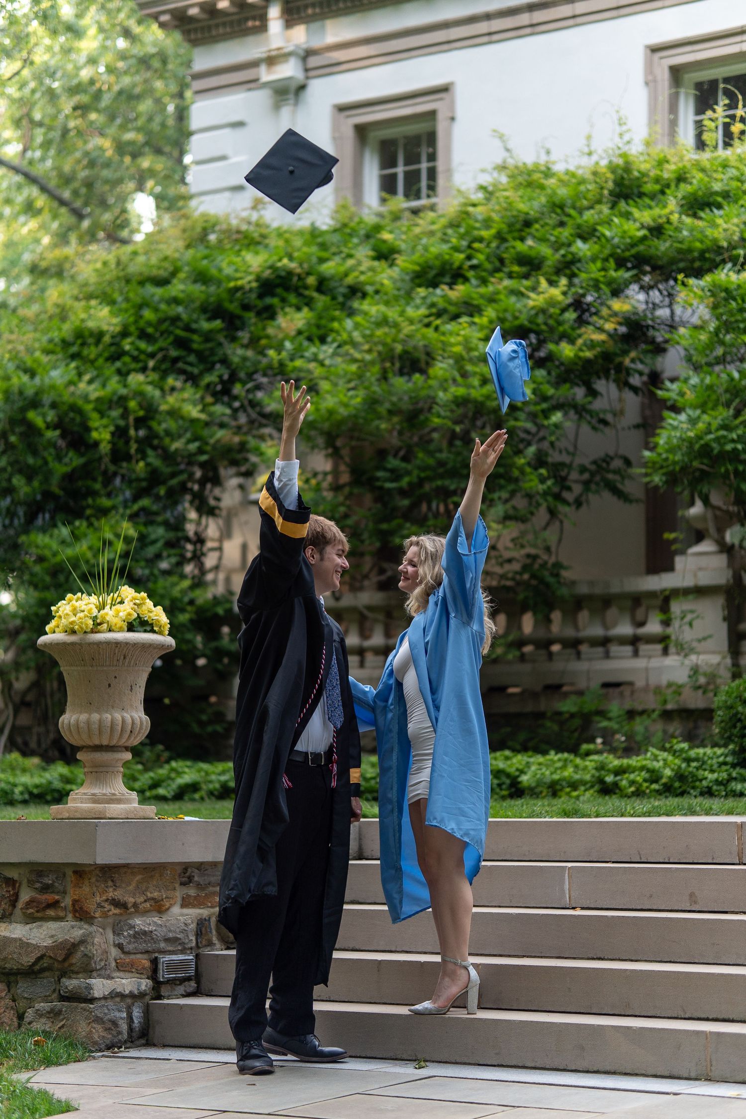 Two graduates in cap and gown joyfully tossing their mortarboard caps in the air outdoors. In Bel Air Maryland