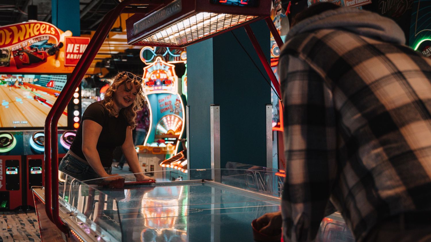 Woman playing air hockey at an arcade while her partner watches from across the table. In Towson Maryland