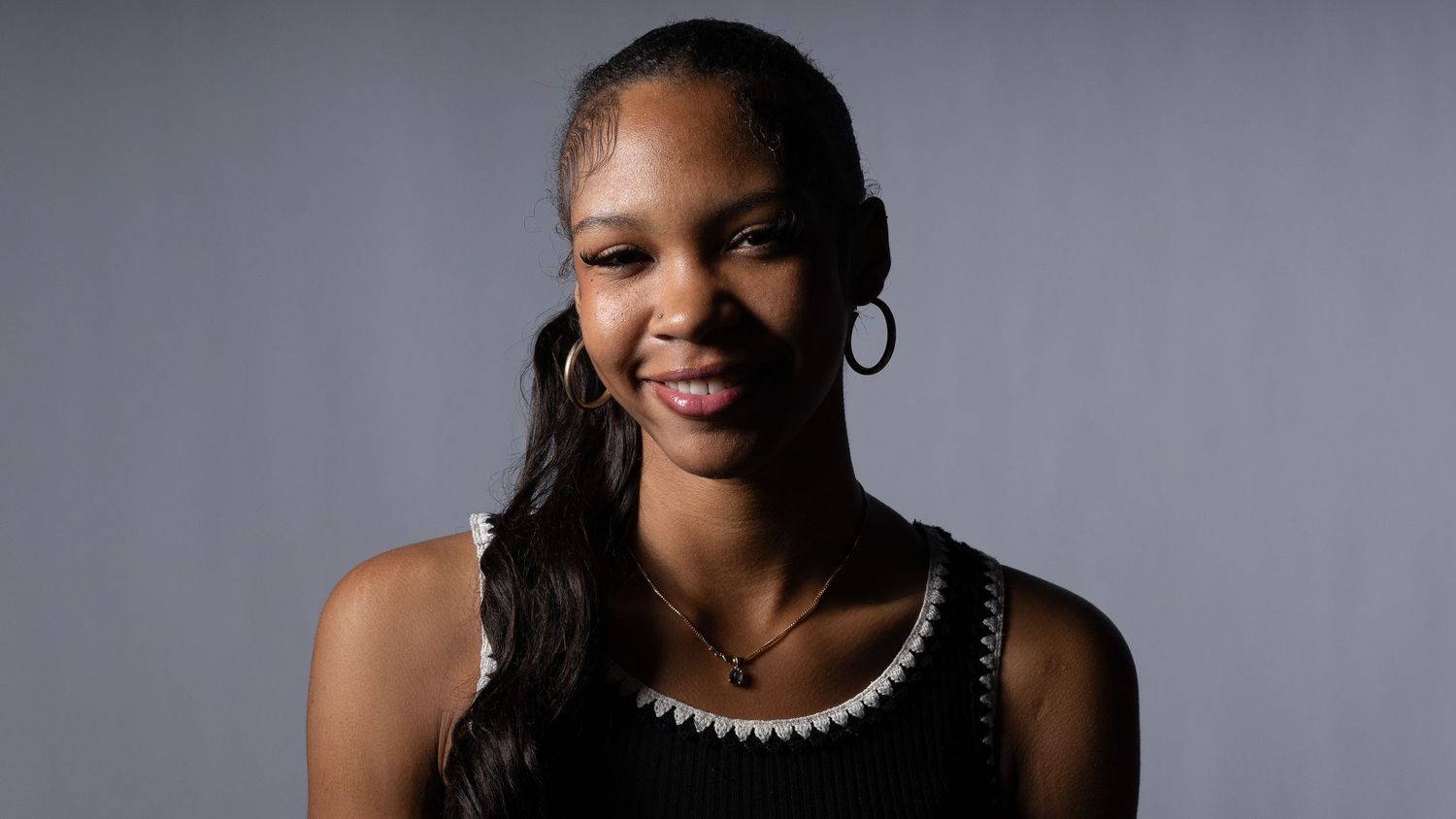 A smiling young woman with hoop earrings and a black top poses against a gray background. In Bel Air Maryland
