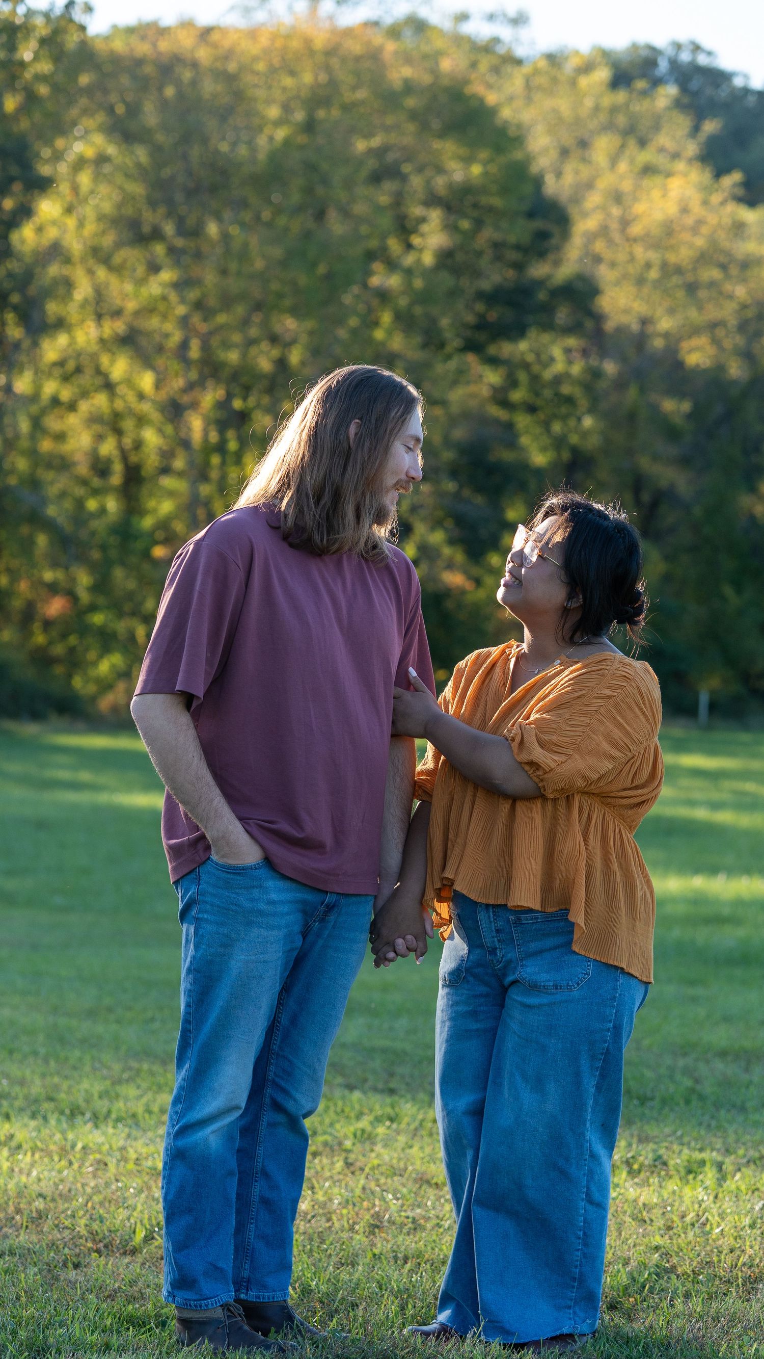 Couple holding hands and gazing at each other in a sunny green park with autumn trees behind. In Jerusalem mill in Fallston Maryland