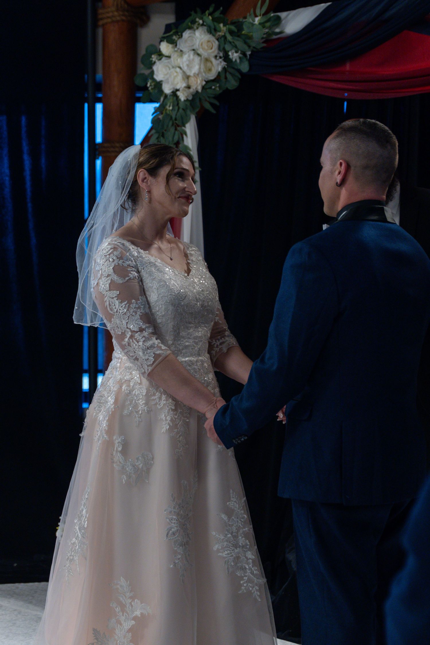 Bride in lace wedding gown holds hands with groom in navy uniform during intimate wedding ceremony.in Abingdon Maryland