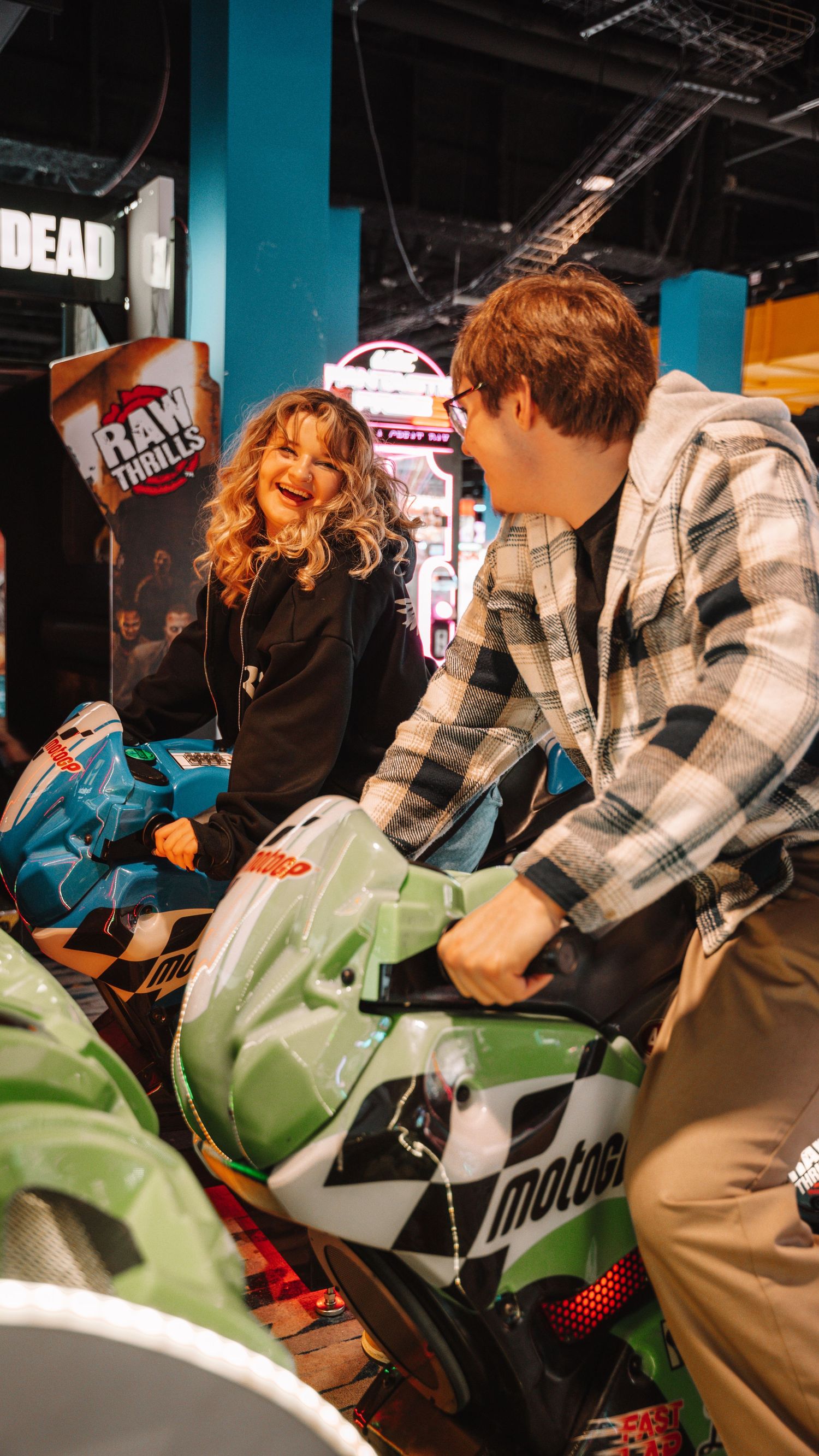 Couple laughing and enjoying a MotoGP motorcycle arcade game at an entertainment venue. In Towson Maryland