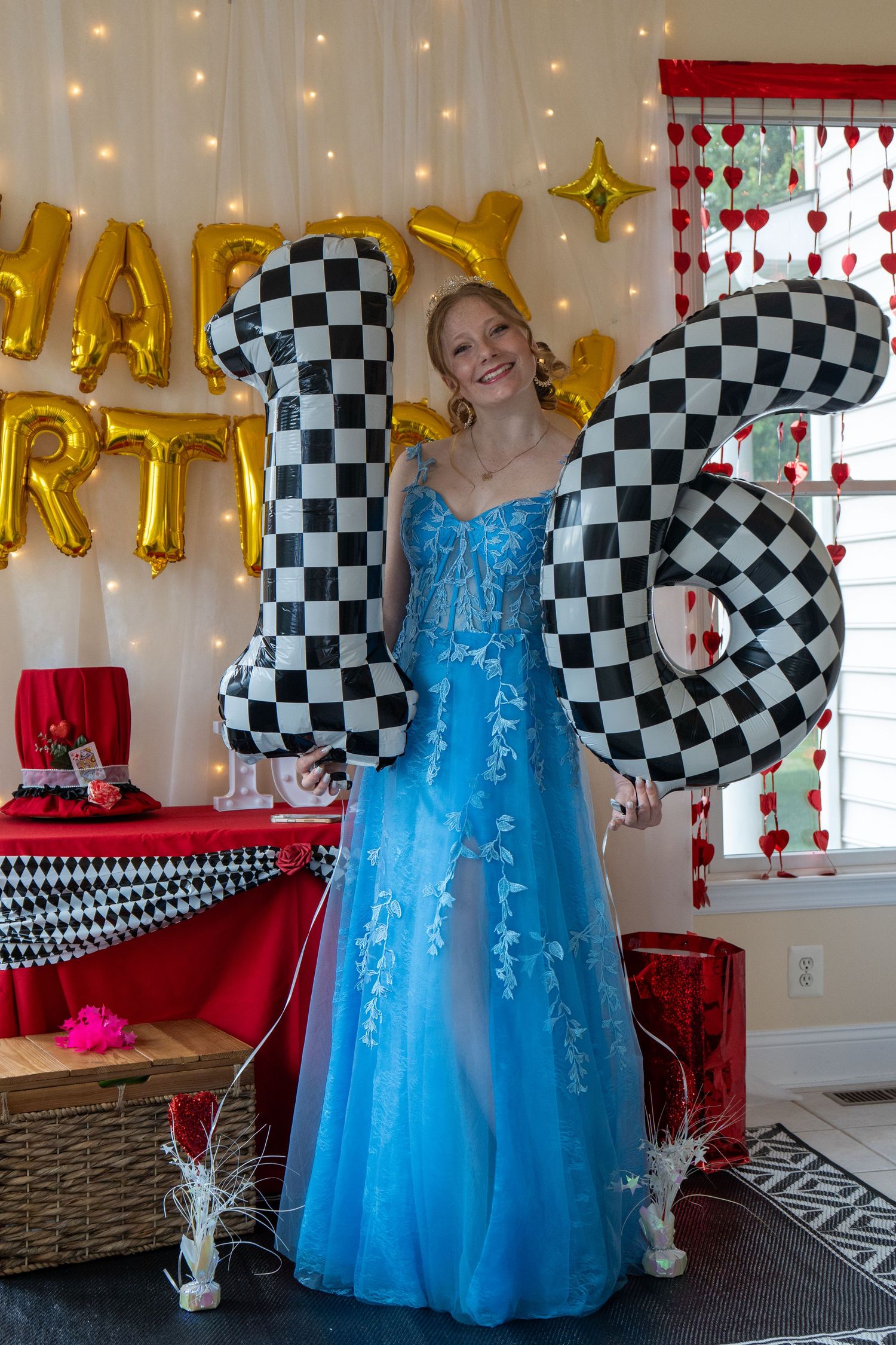 Teen girl in blue lace gown holding checkered number 16 balloons at a sweet sixteen birthday party. In Bel Air Maryland