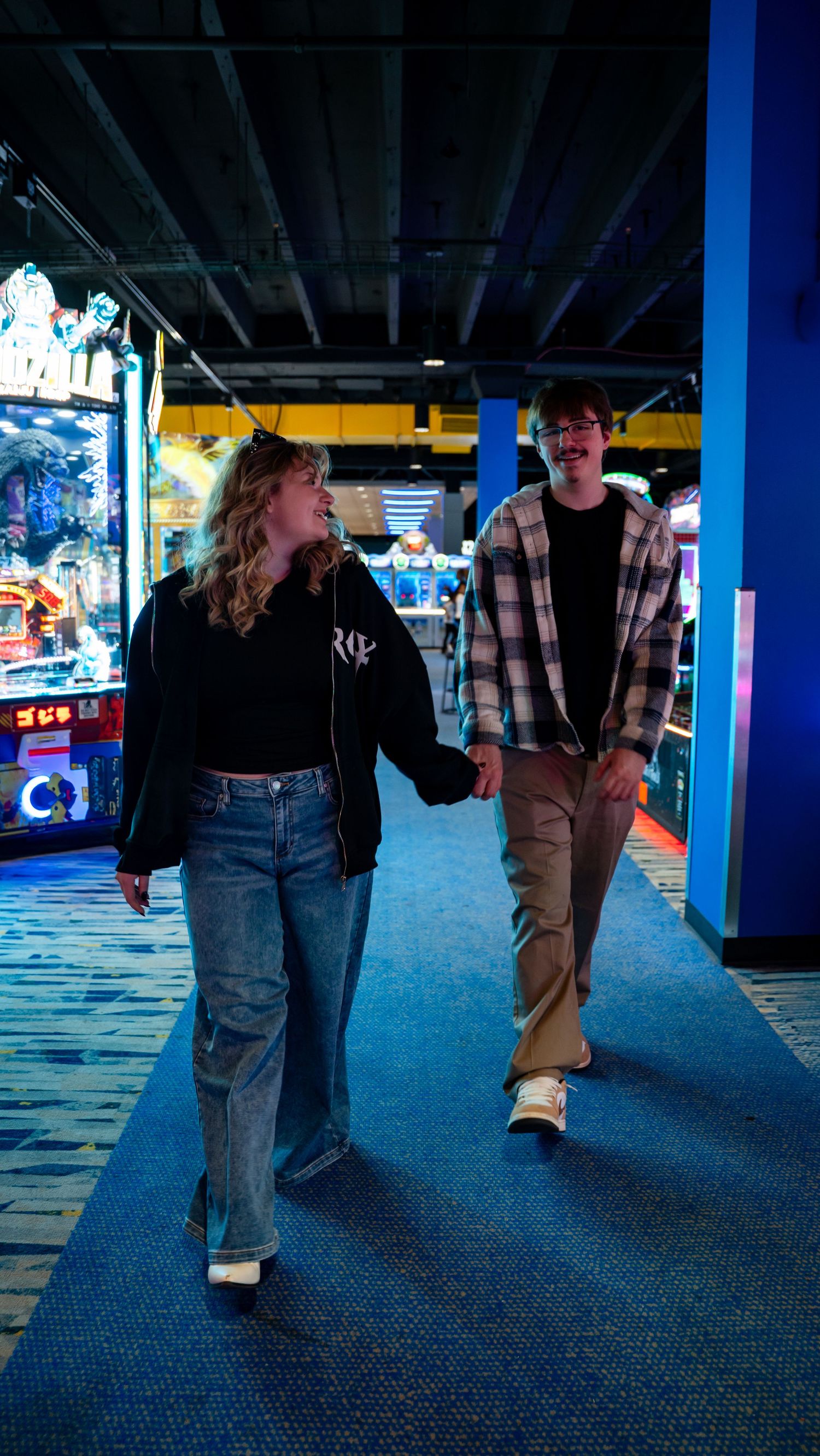 Happy couple holding hands and walking together through a vibrant neon-lit arcade. In Towson Maryland