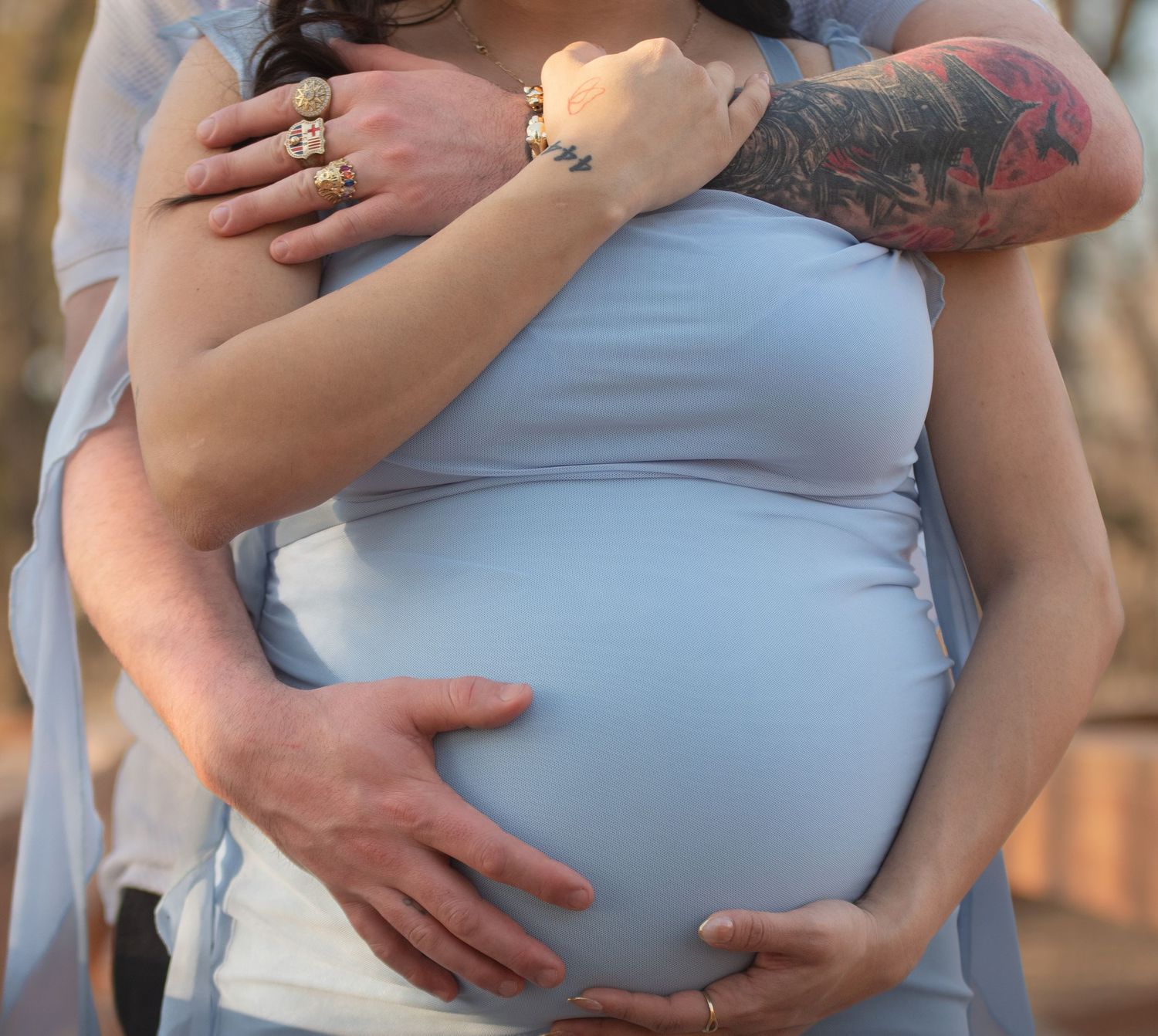 Close-up of a couple's hands embracing a maternity bump in a light blue dress, Grand Island, Nebraska.