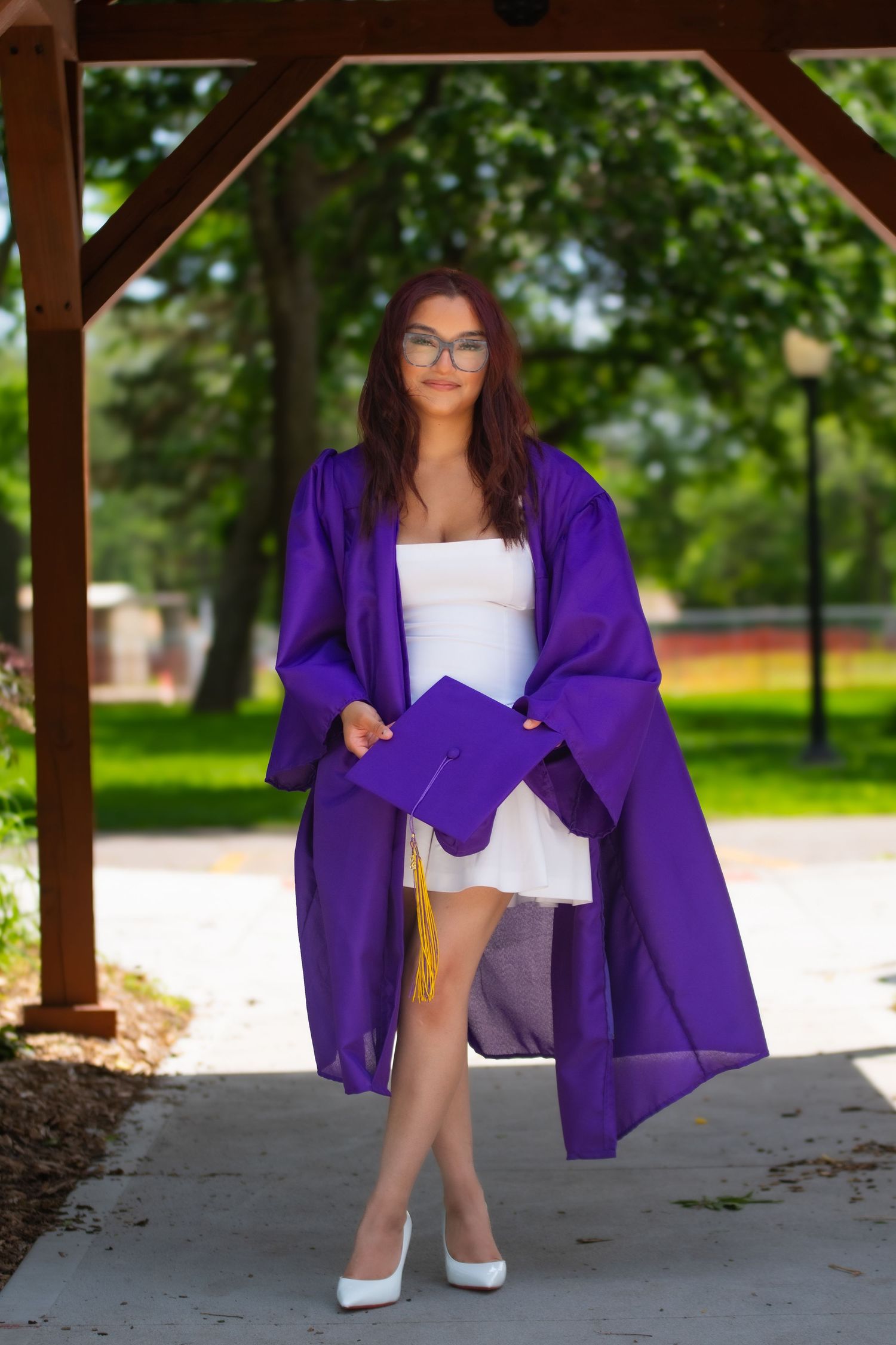 True to color image of high school senior in cap and gown standing with one leg crossed.