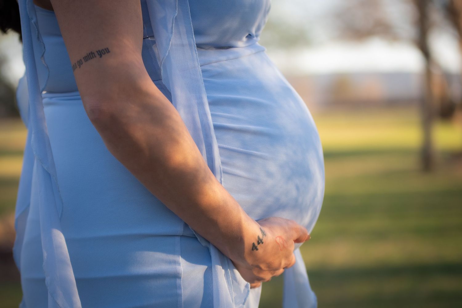 Full-length, true-to-color maternity portrait of a woman in a blue dress at Hall County Park, Grand Island, NE.