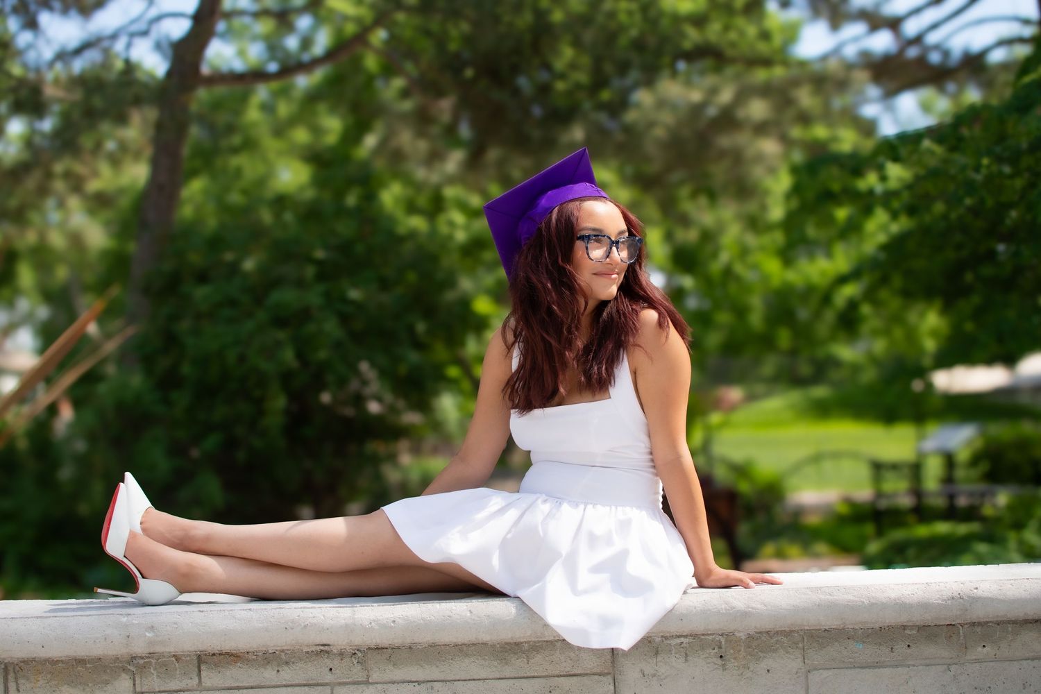 High school senior in white dress and purple cap sitting at Hall County Park in Grand Island, Nebraska.