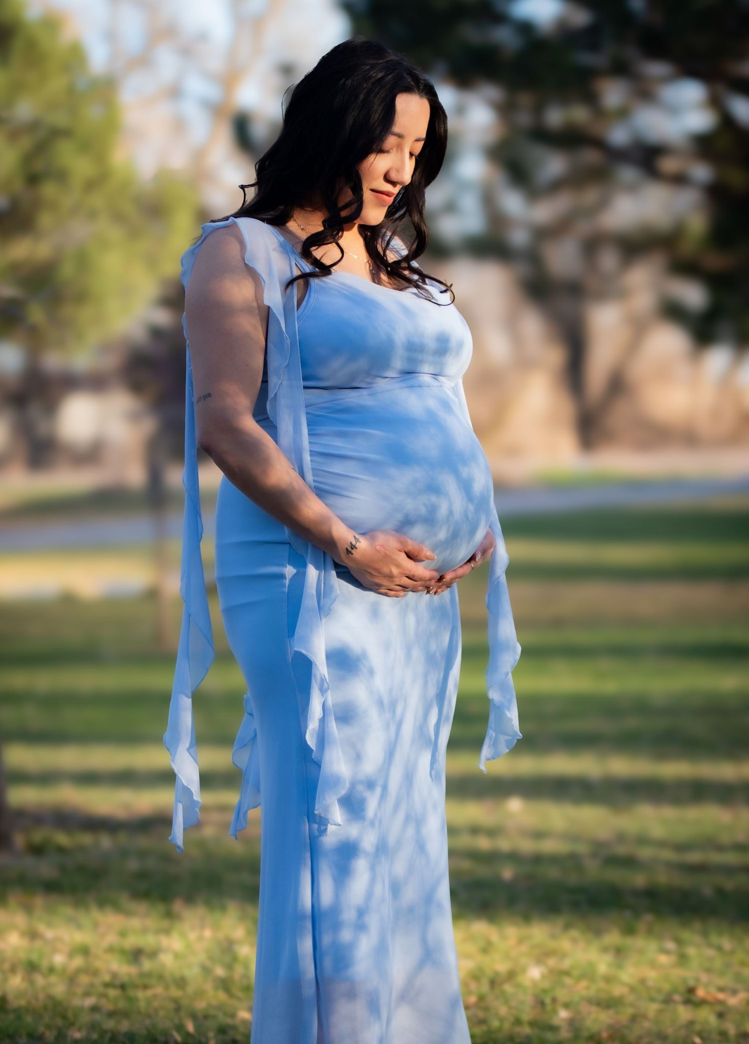 Clean side-profile shot of a pregnant woman's baby bump in a blue dress at Hall County Park, Nebraska.