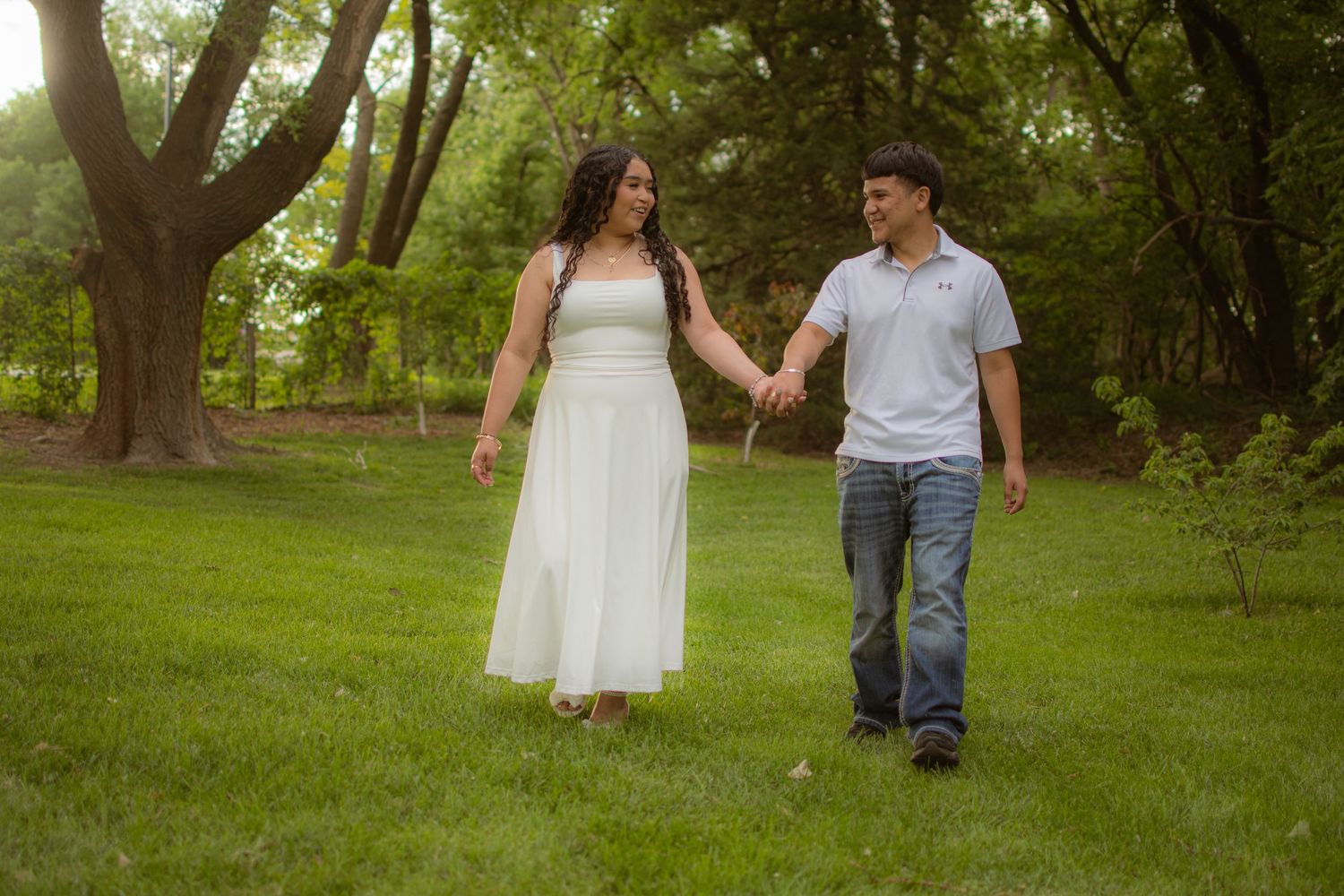 True to color natural portrait of a young couple smiling while holding hands and walking across a grassy field at Hall County Park in Grand