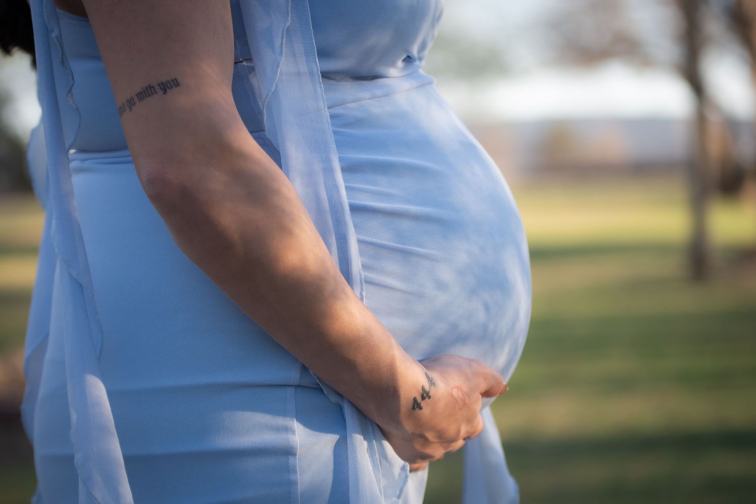 Close up shot of photo session picture of mother in blue holding her belly under the sunset.