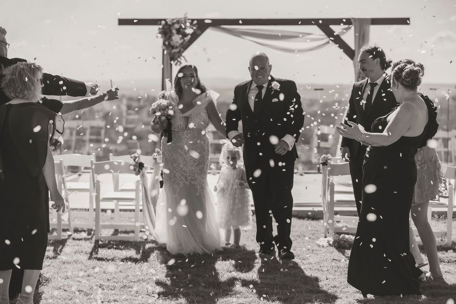 Black and white wedding photo of bride and groom walking down aisle as guests toss confetti outdoors Keteka Hill Toowoomba wedding photos