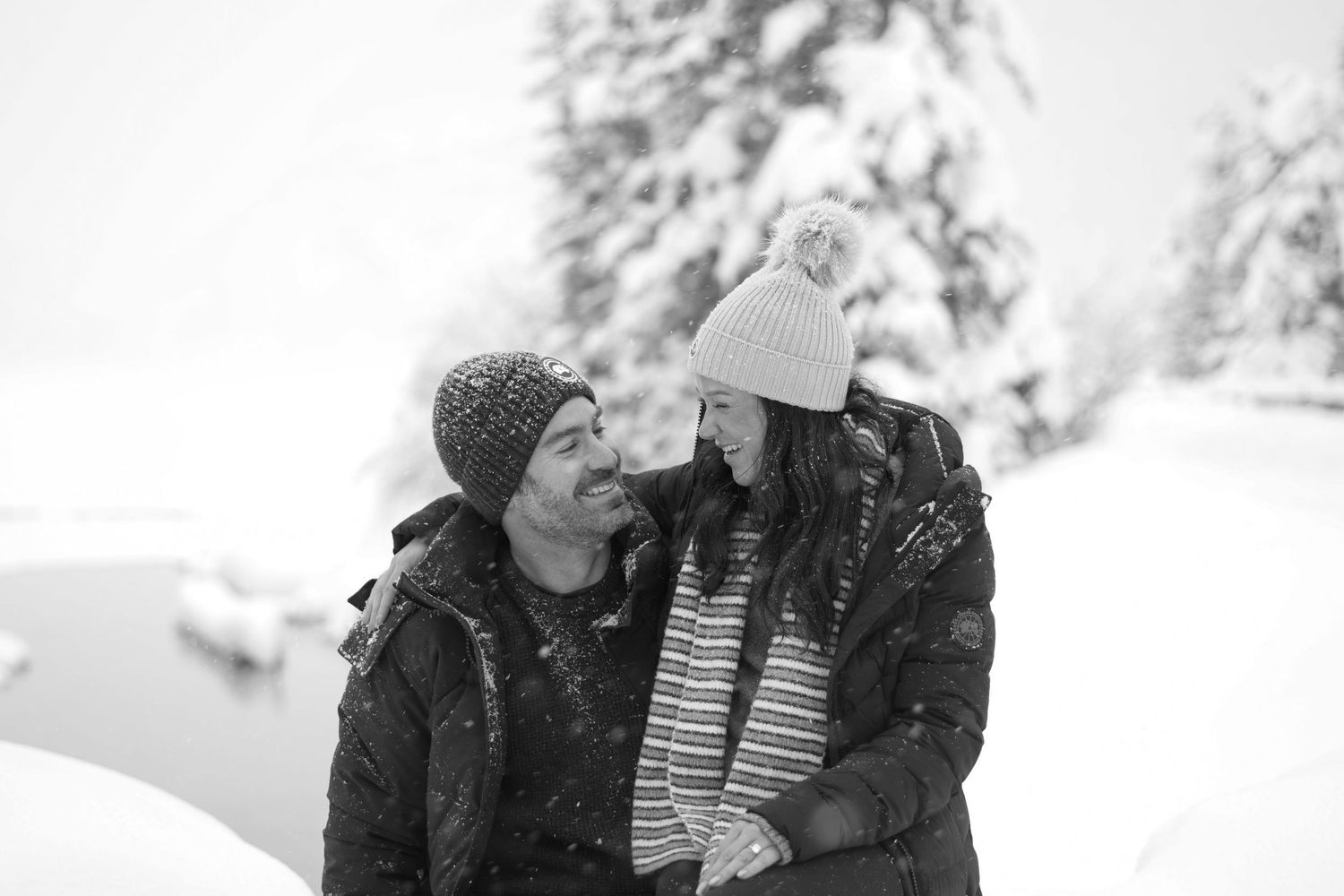 Couple siting together with a river and snow covered trees behind them